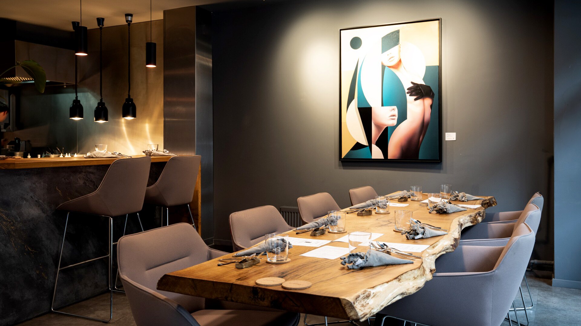 In einem Restaurant steht ein gedeckter Tisch mit Stühlen, an der Wand hängt ein Kunstwerk.