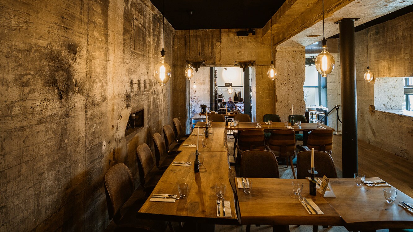 In einem Restaurant mit rustikalen Wänden aus Beton stehen Stühle an Holzstühlen.