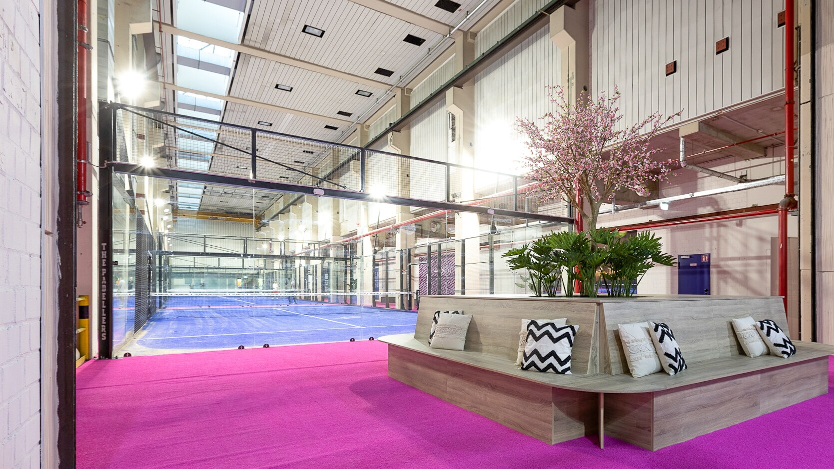 Vor einem Indoor-Tennisplatz liegt ein pinker Teppich, auf dem eine Sitzecke steht.
