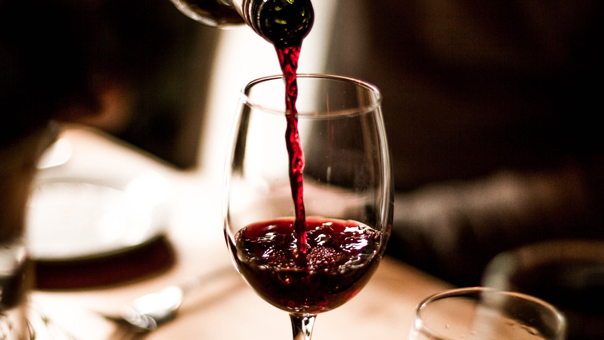 Nahaufnahme eines Weinglases, in das Rotwein eingeschenkt wird.