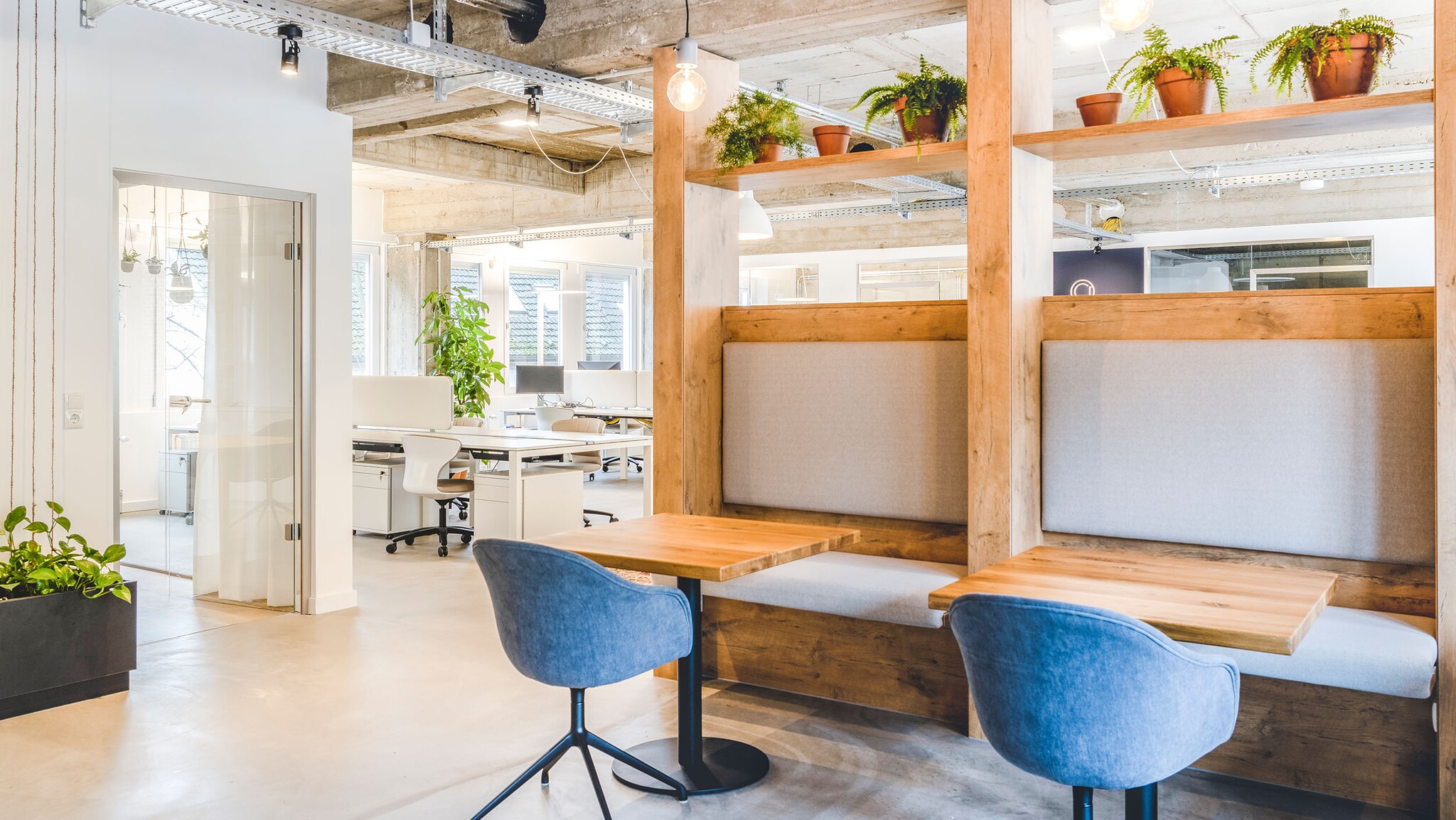 Eine helle Bürofläche mit Holztischen und Bänken sowie Stühlen und mehreren Bürotischen im Hintergrund.