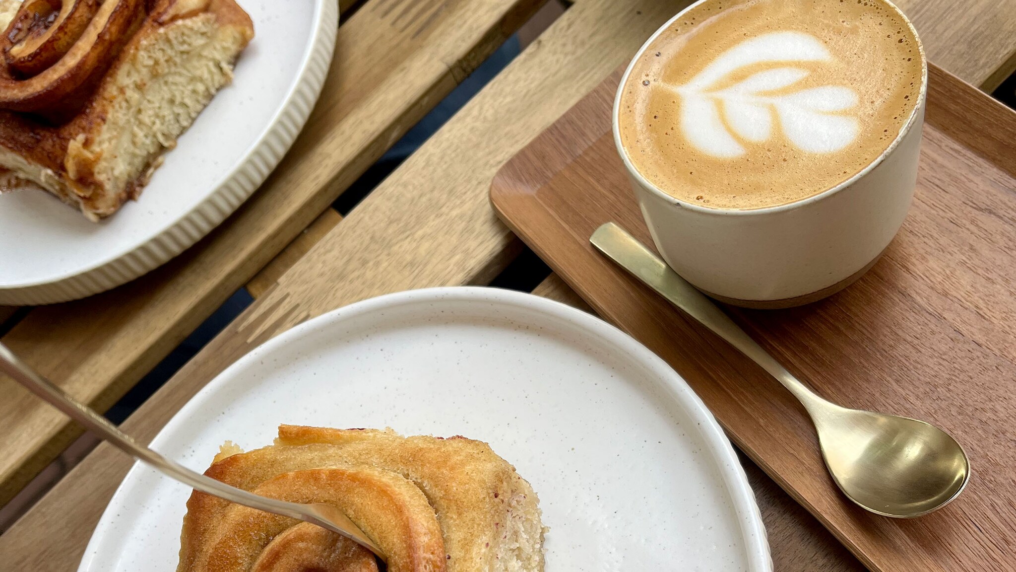 Ein Cappuccino und eine Zimtschnecke stehen auf einem Holztisch.