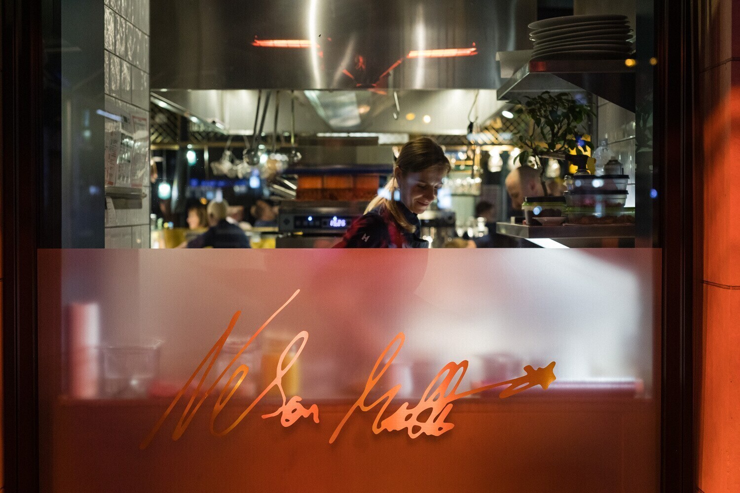 Hinter der roten Glasscheibe eines Restaurants steht eine Person in der Küche.
