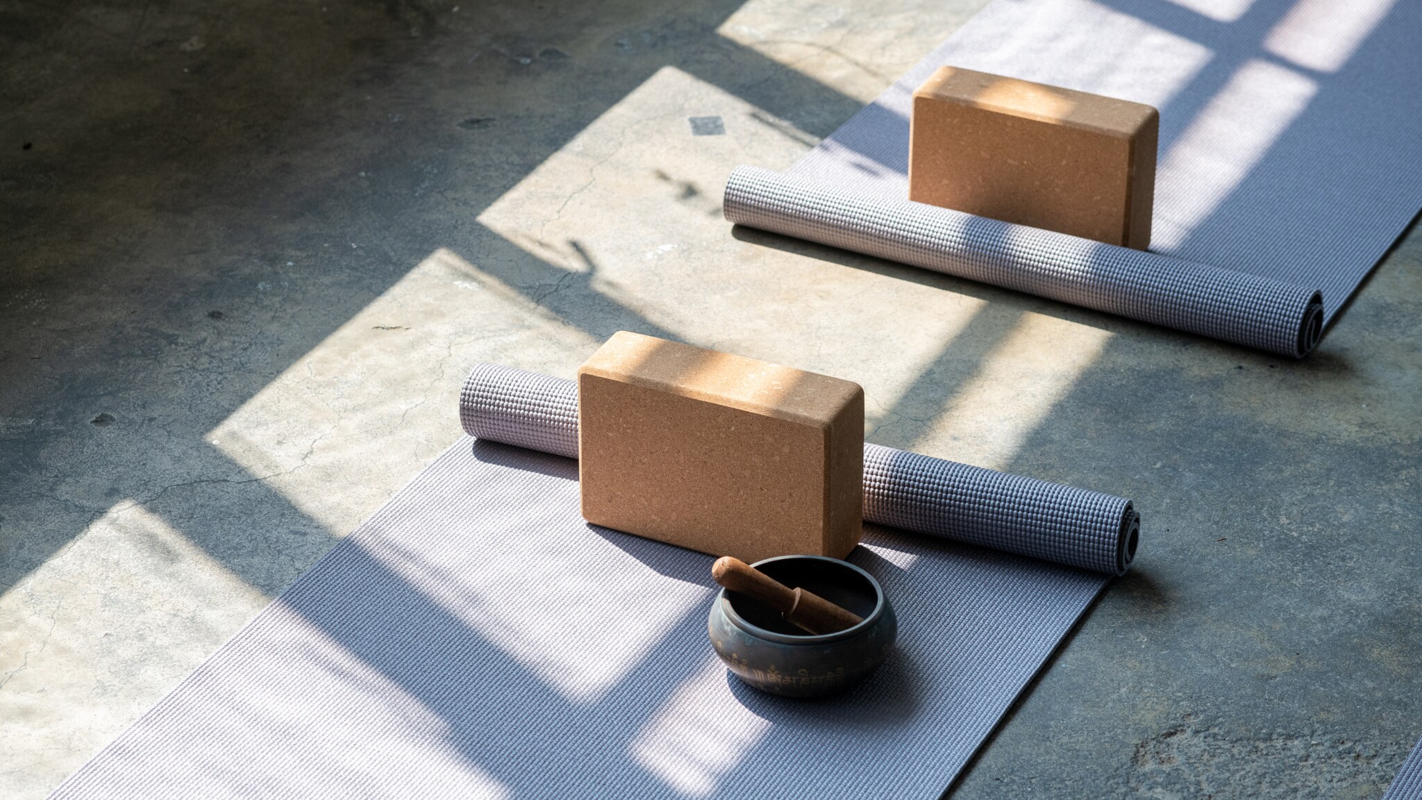 Zwei halb aufgerollte Yogamatten auf einem Steinboden mit Blöcken und einer Klangschale.
