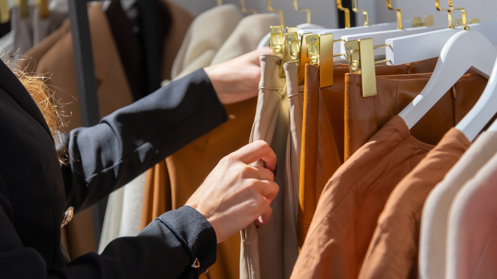 Nahaufnahme einer Person, die eine aufgehängte Hose an einem Kleiderbügel in den Händen hält, die neben weiteren Kleidungsstücken hängt.