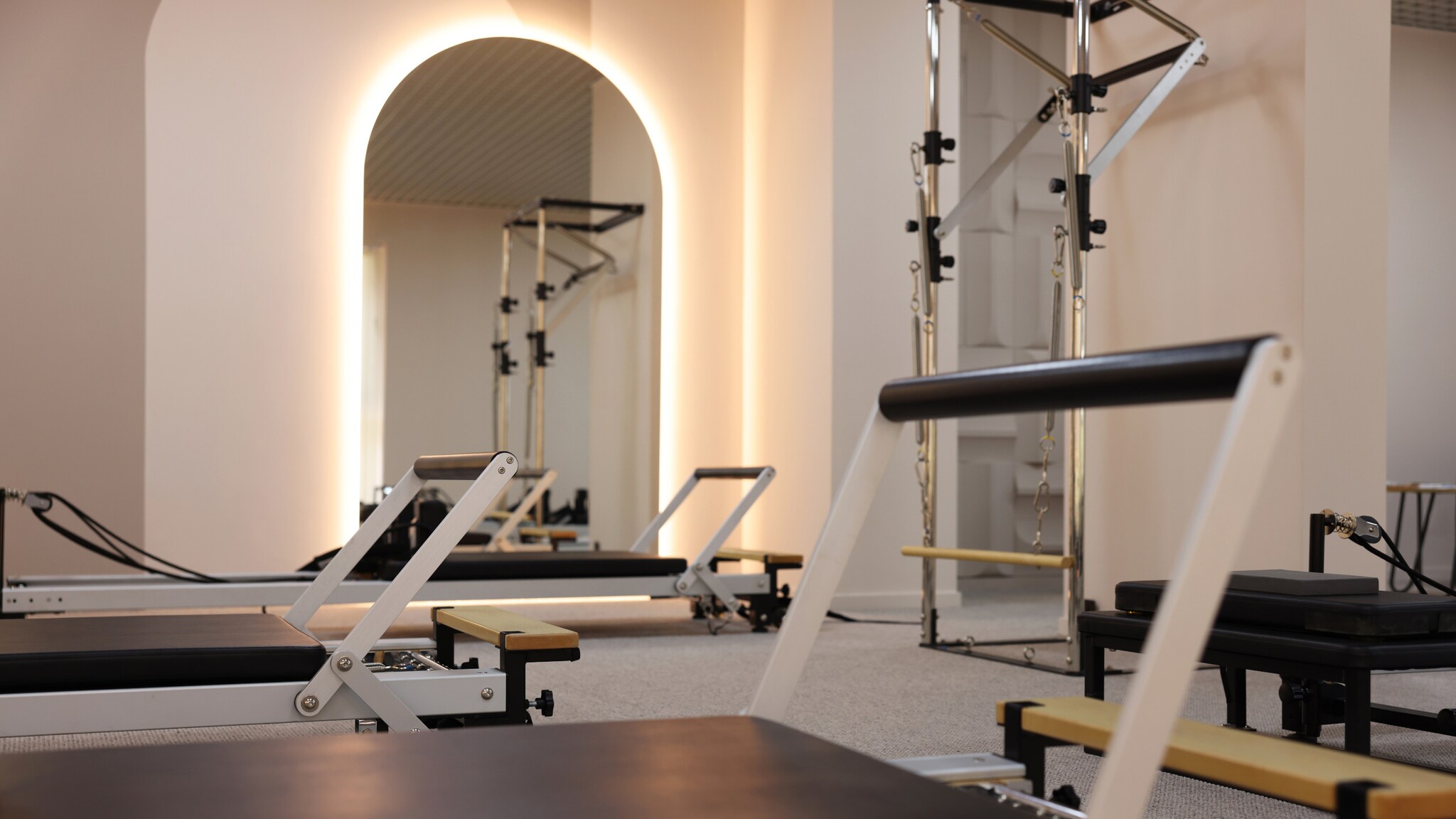 Ein Raum in dem mehrere Reformer-Pilates-Sportgeräte stehen, im Hintergrund ein halbrunder Spiegel mit dezenter Beleuchtung.