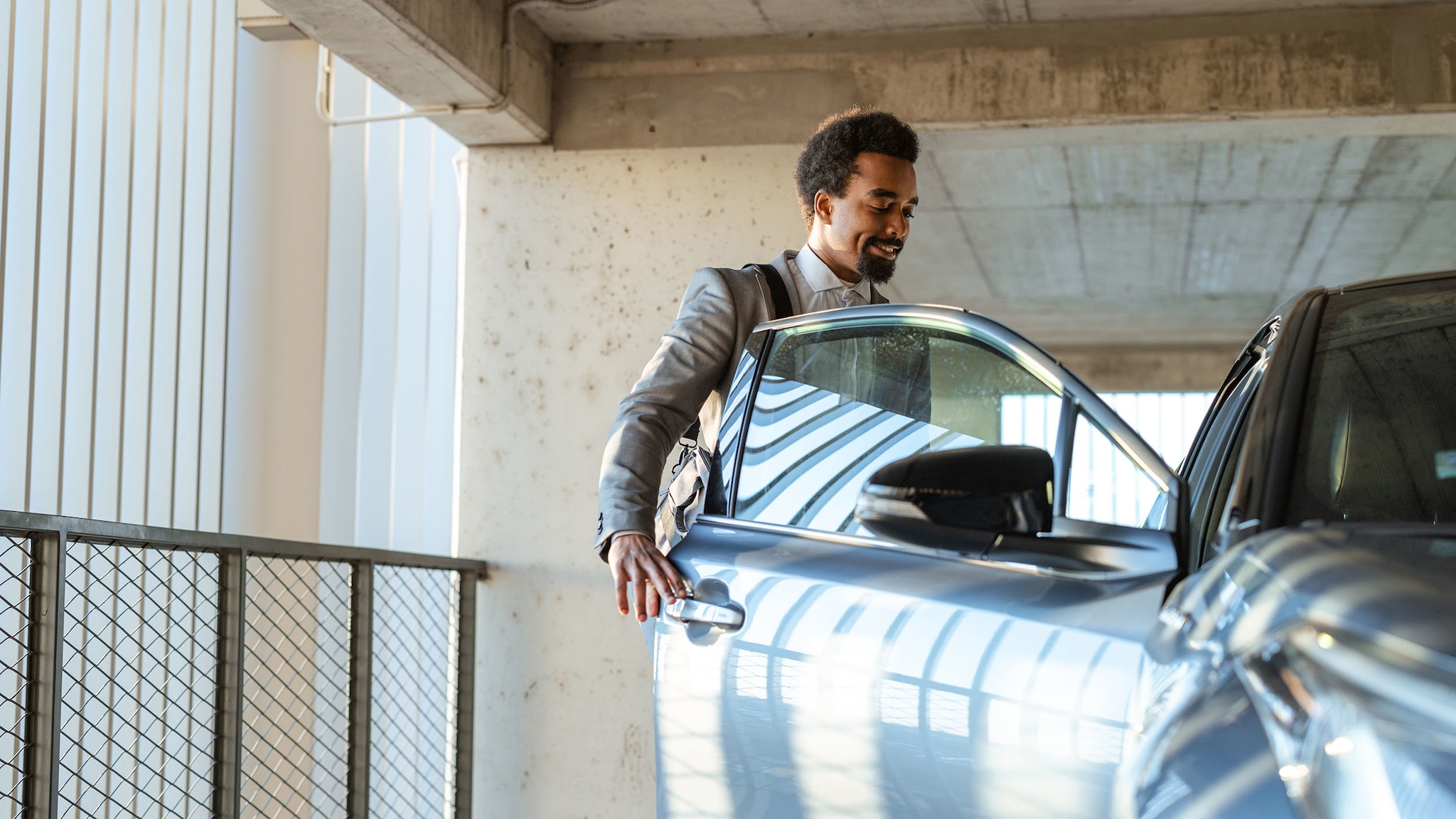 Sixt+ auto abo für Amex Business Ein Mann steht in einem Parkhaus und öffnet die Tür eines Autos.