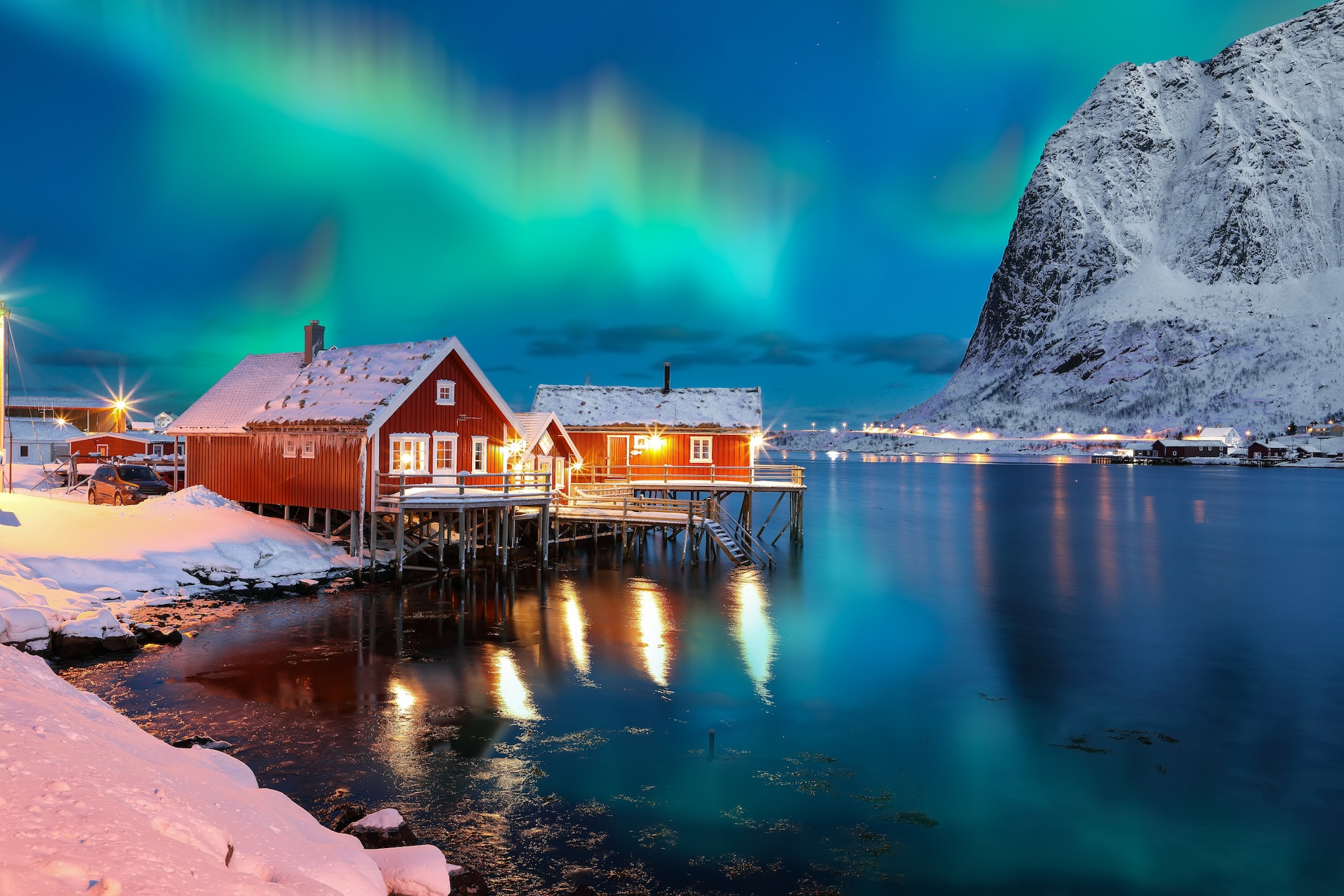 Rote Häuschen in einer verschneiten Landschaft mit See und Bergen, am Himmel Polarlichter.