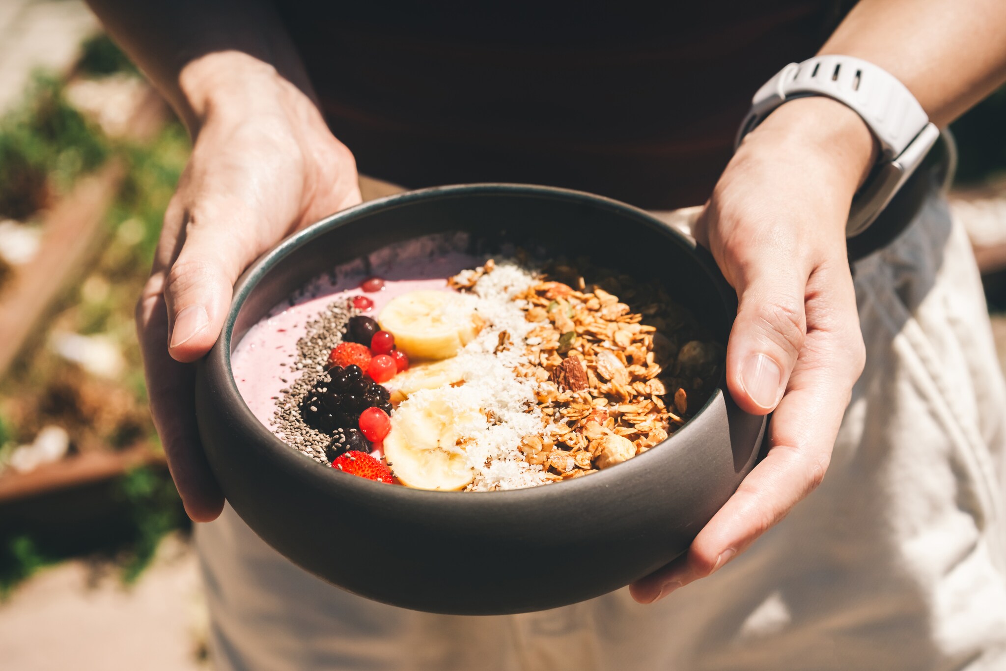 Eine Person hält eine Schale mit ballaststoffreichem Granola mit Chiasamen, Beeren und Bananen in beiden Händen. 