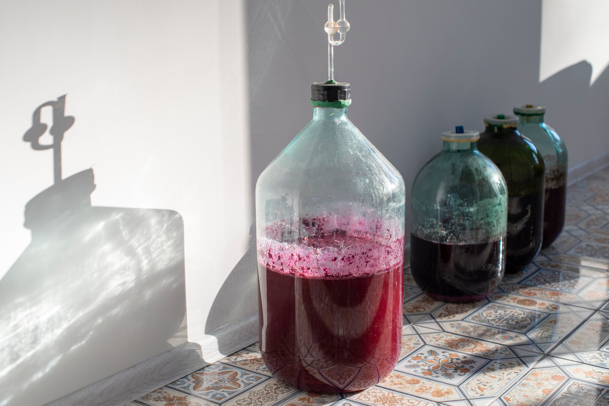 Gärbehälter aus Glas mit Rotwein, die auf einem gefliesten Boden stehen.