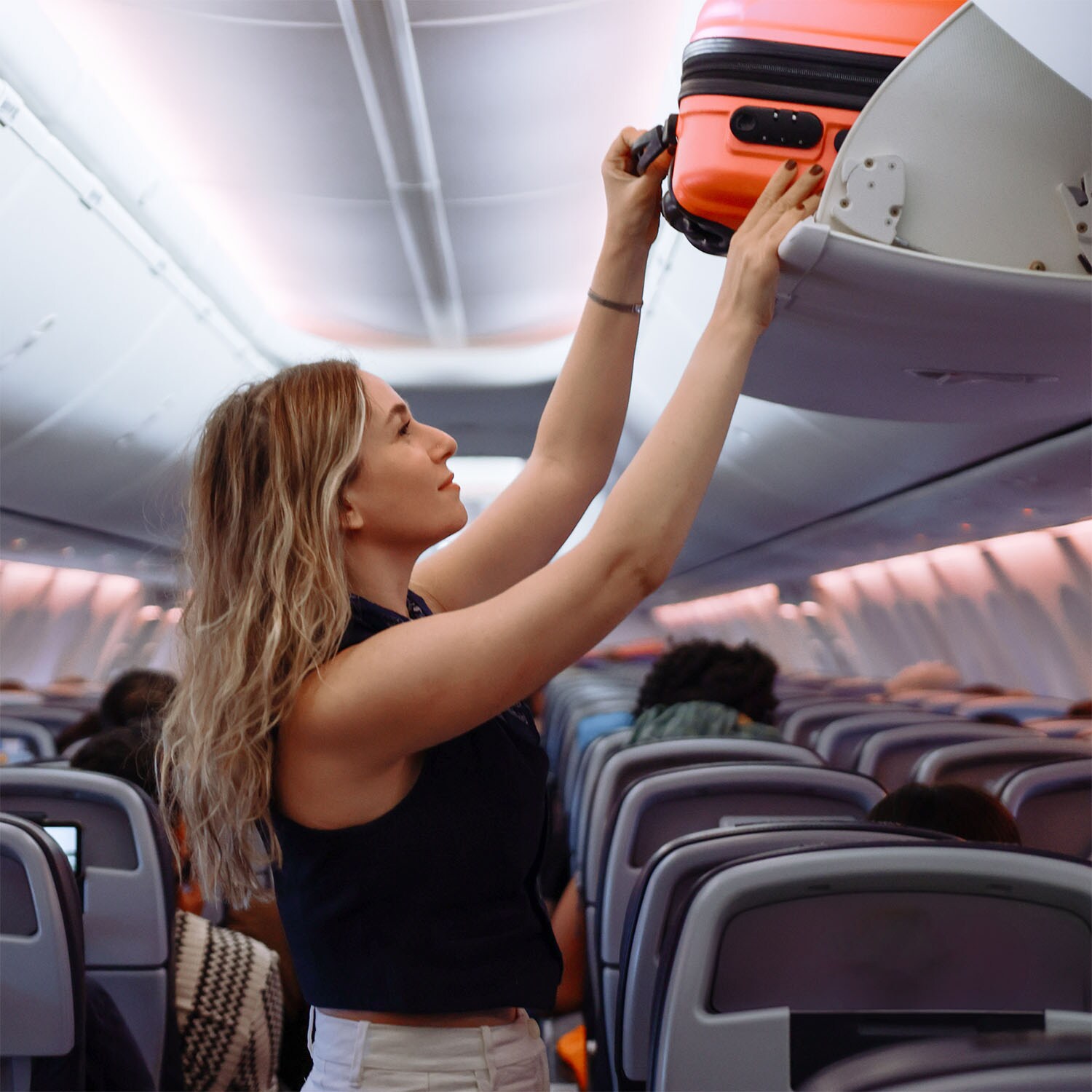 Eine Frau schiebt einen Koffer ins Gepäckfach in einem Flugzeug.