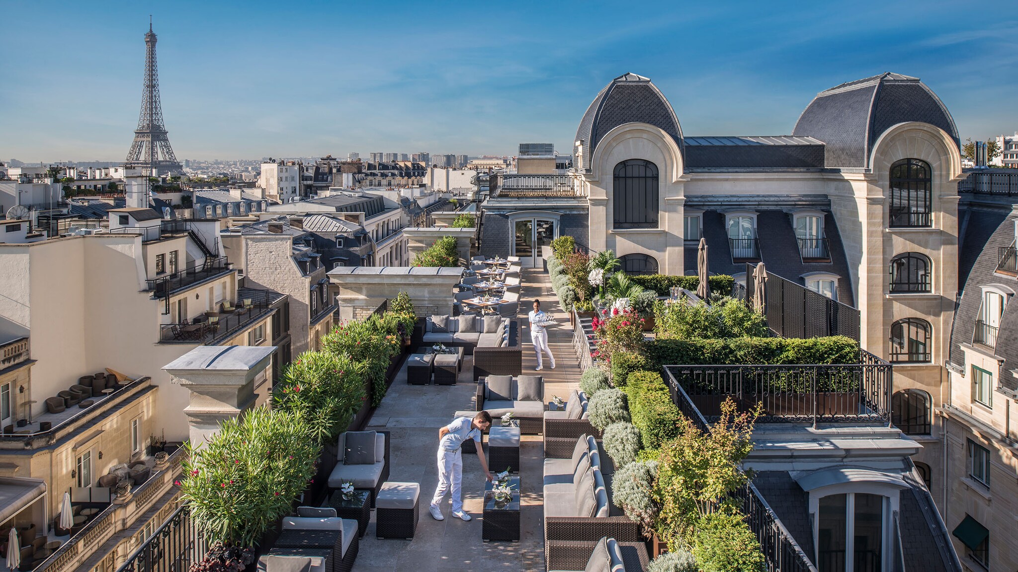 Auf einer sehr großen Dachterrasse stehen Tische und Stühle, im Hintergrund sieht man den Eiffelturm.