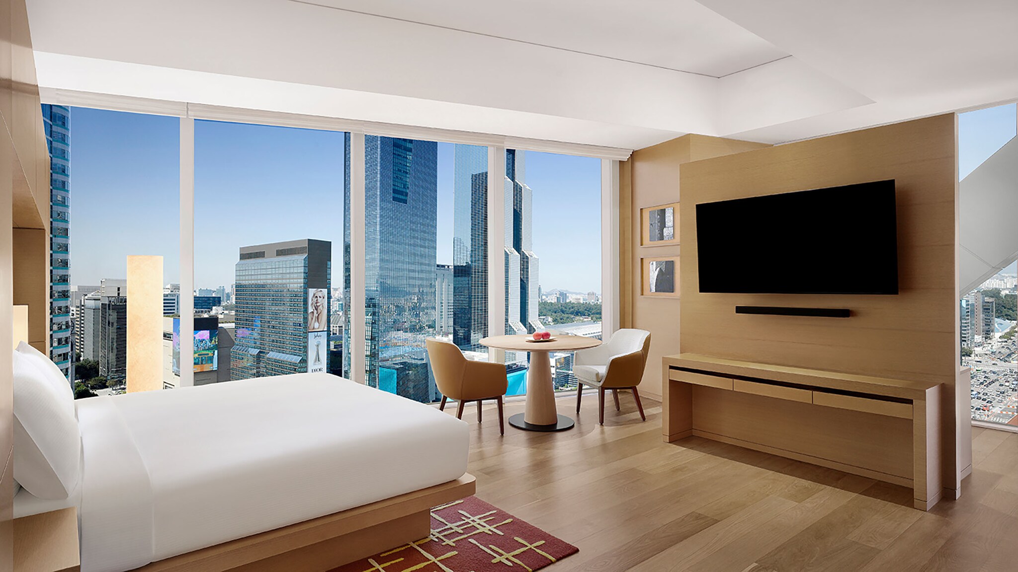 In einer Hotelsuite steht ein Bett vor einem bodentiefen Fenster mit Blick auf eine Großstadt.