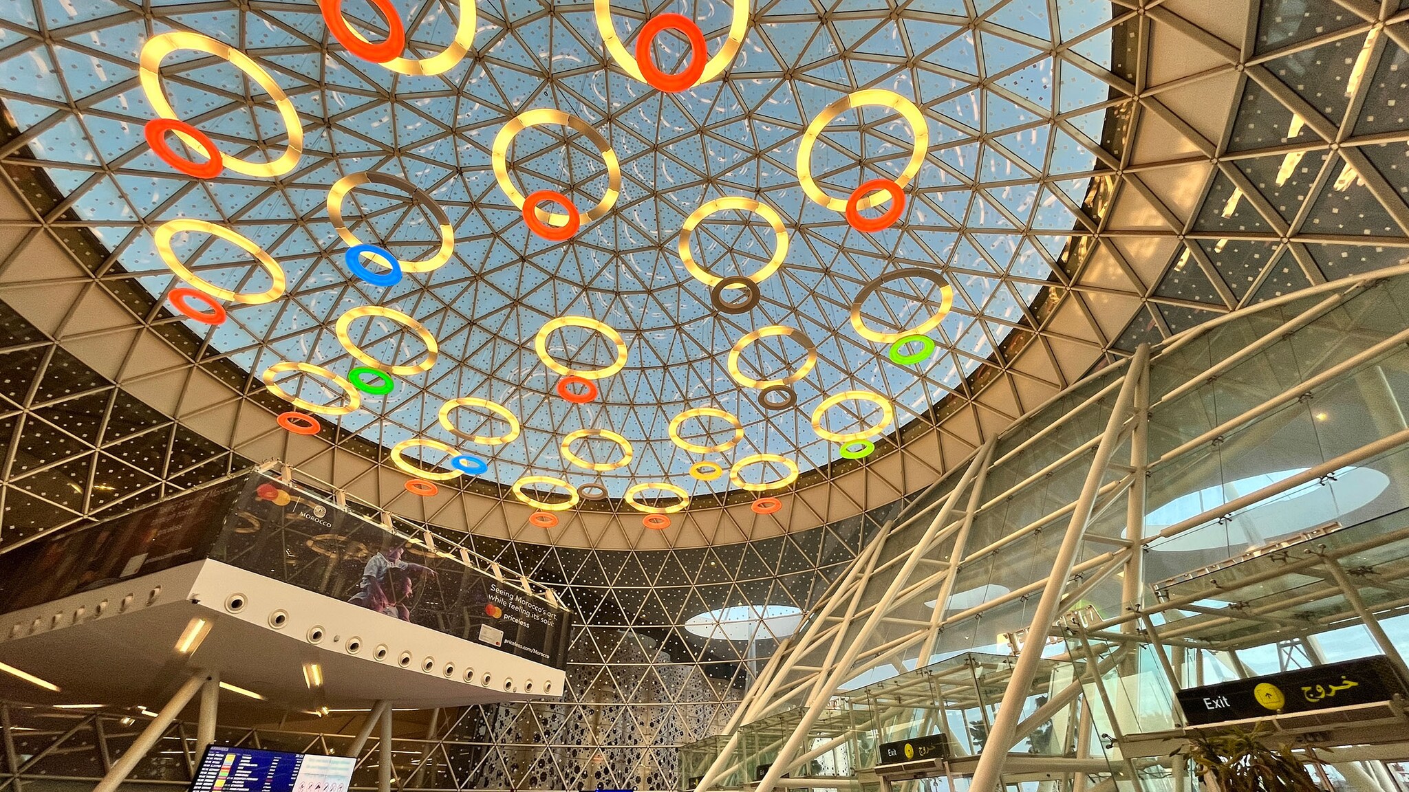 Glaskuppel mit kreisförmigen Lichtskulpturen in einem Flughafenterminal.