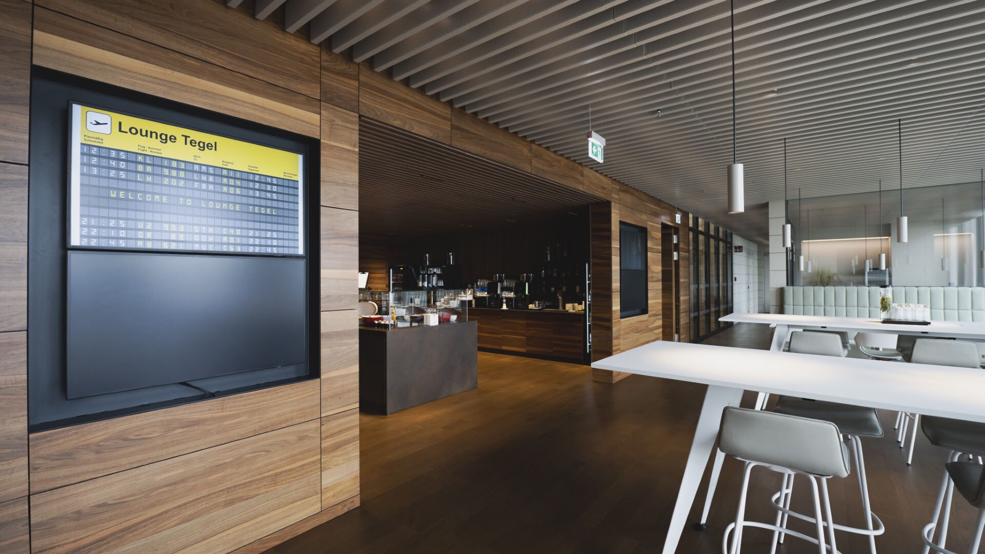 Moderne Flughafen-Lounge mit Tischen und Barbereich,  im Vordergrund auf einer Anzeigetafel die Aufschrift Berlin Tegel.
