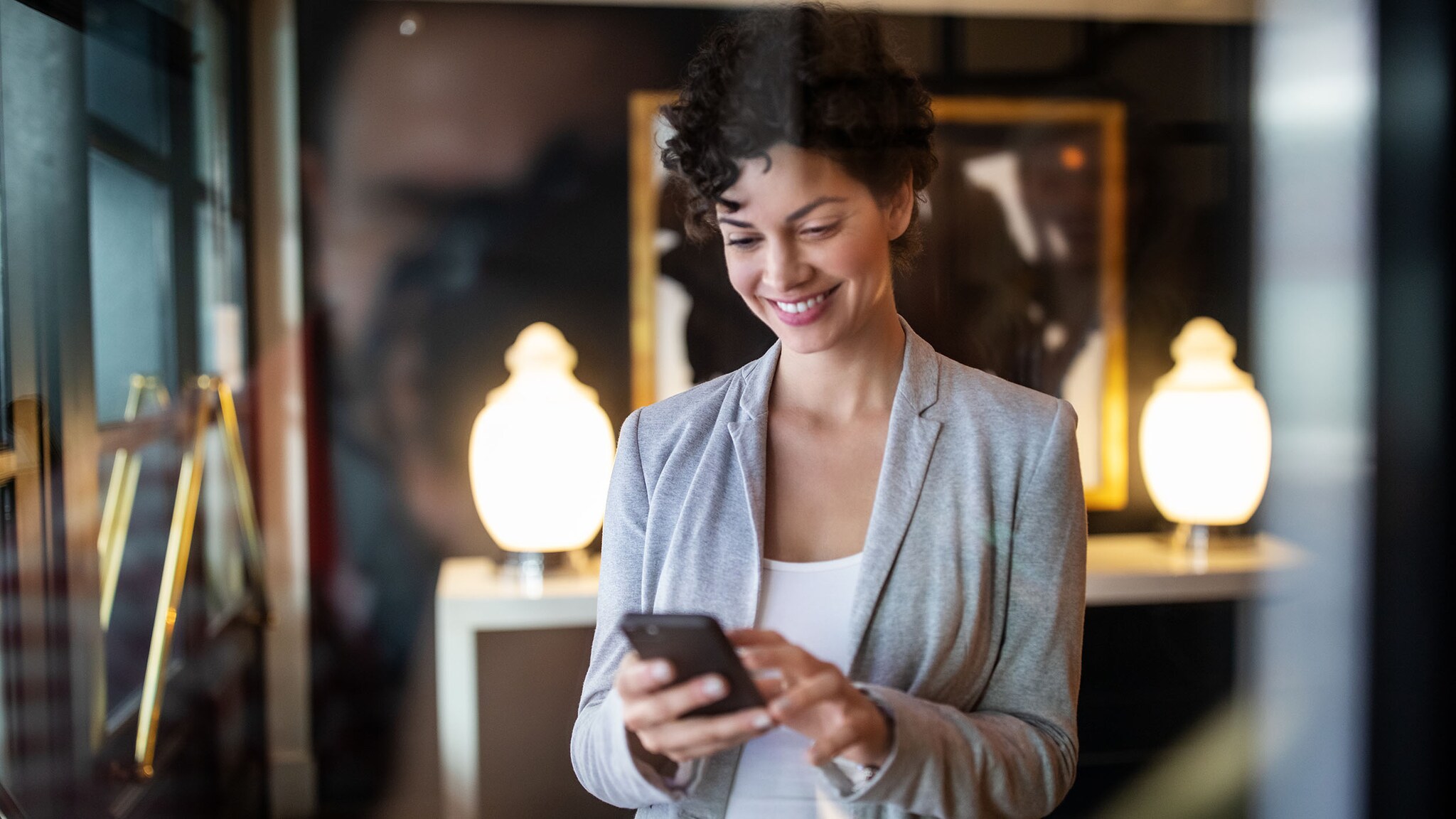 Eine Frau steht in einem Hotelzimmer und schaut auf ihr Smartphone.