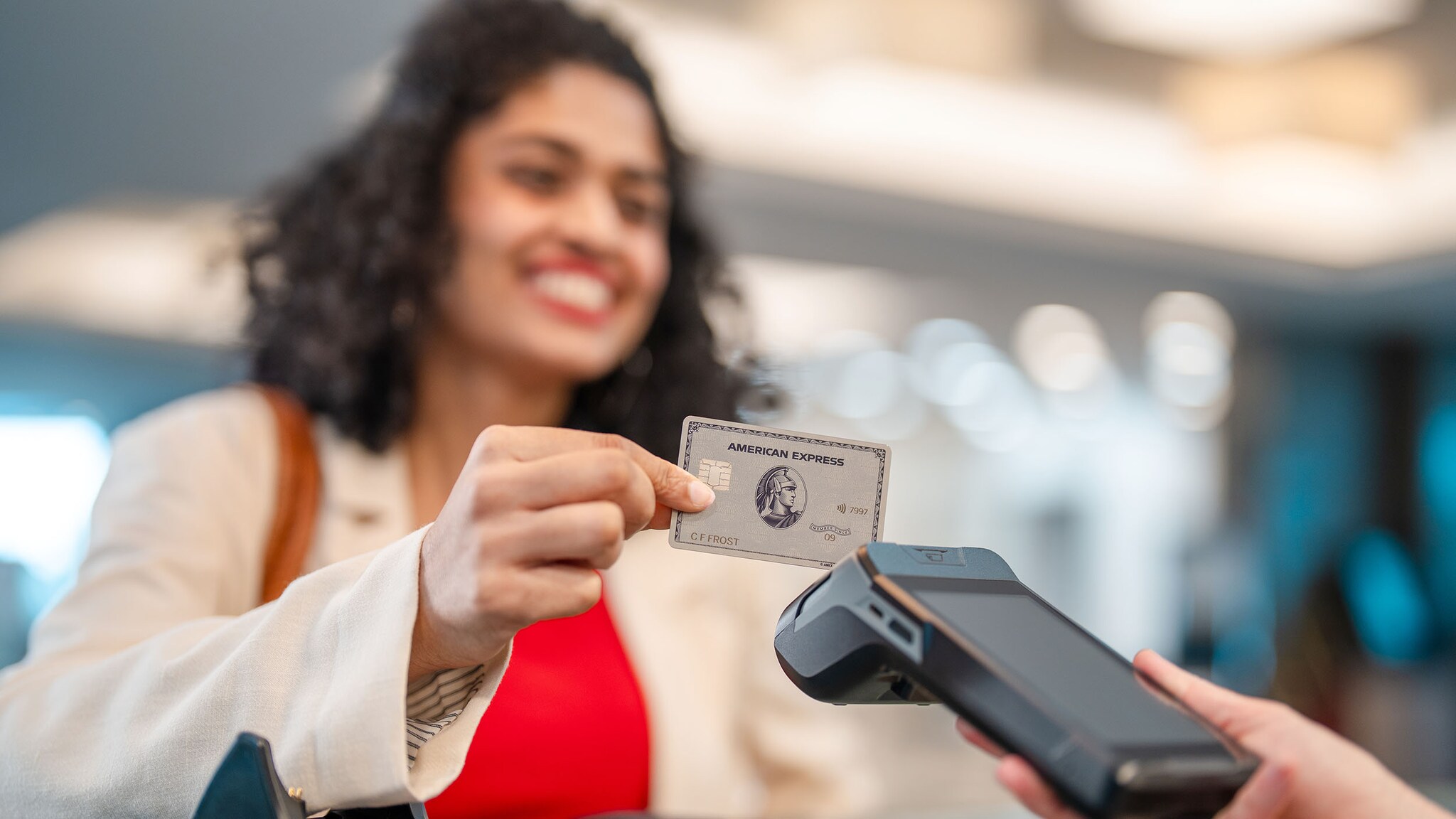 Eine Frau hält eine Kreditkarte von American Express an ein Kartenlesegerät.