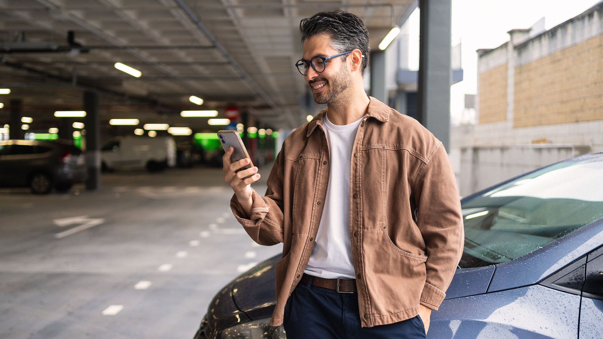 Ein Mann lehnt an einem Auto und schaut auf sein Smartphone.