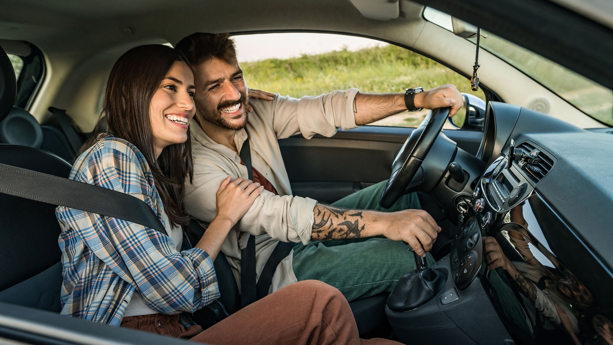 Ein Mann und eine Frau sitzen in einem fahrenden Auto und lachen. 