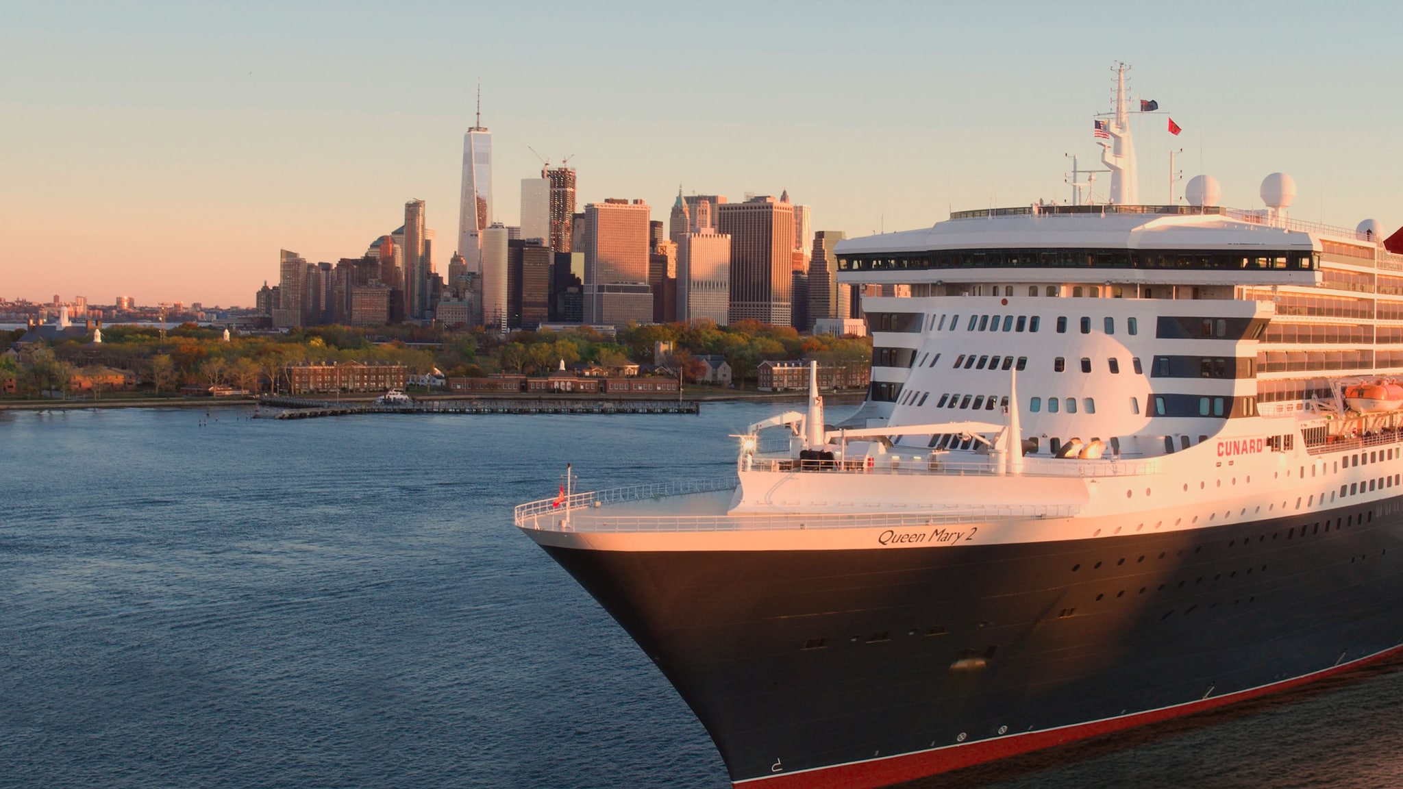 Das Kreuzfahrtschiff Queen Mary 2 fährt an der Skyline einer Stadt vorbei.