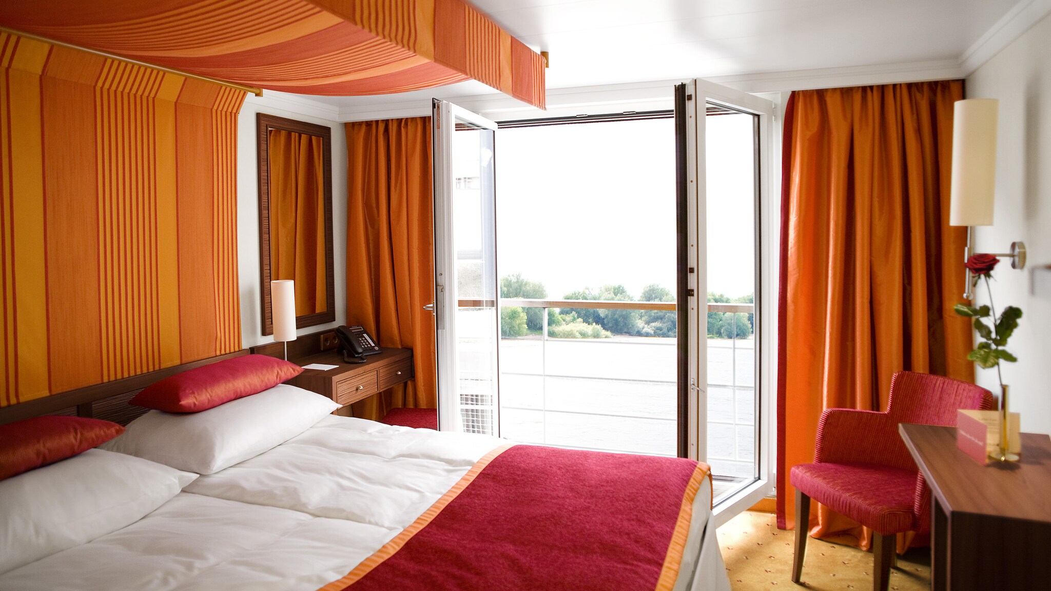 In der Kabine eines Fluss-Kreuzfahrtschiffes sthet ein großes Bett vor einer Terrassentür.