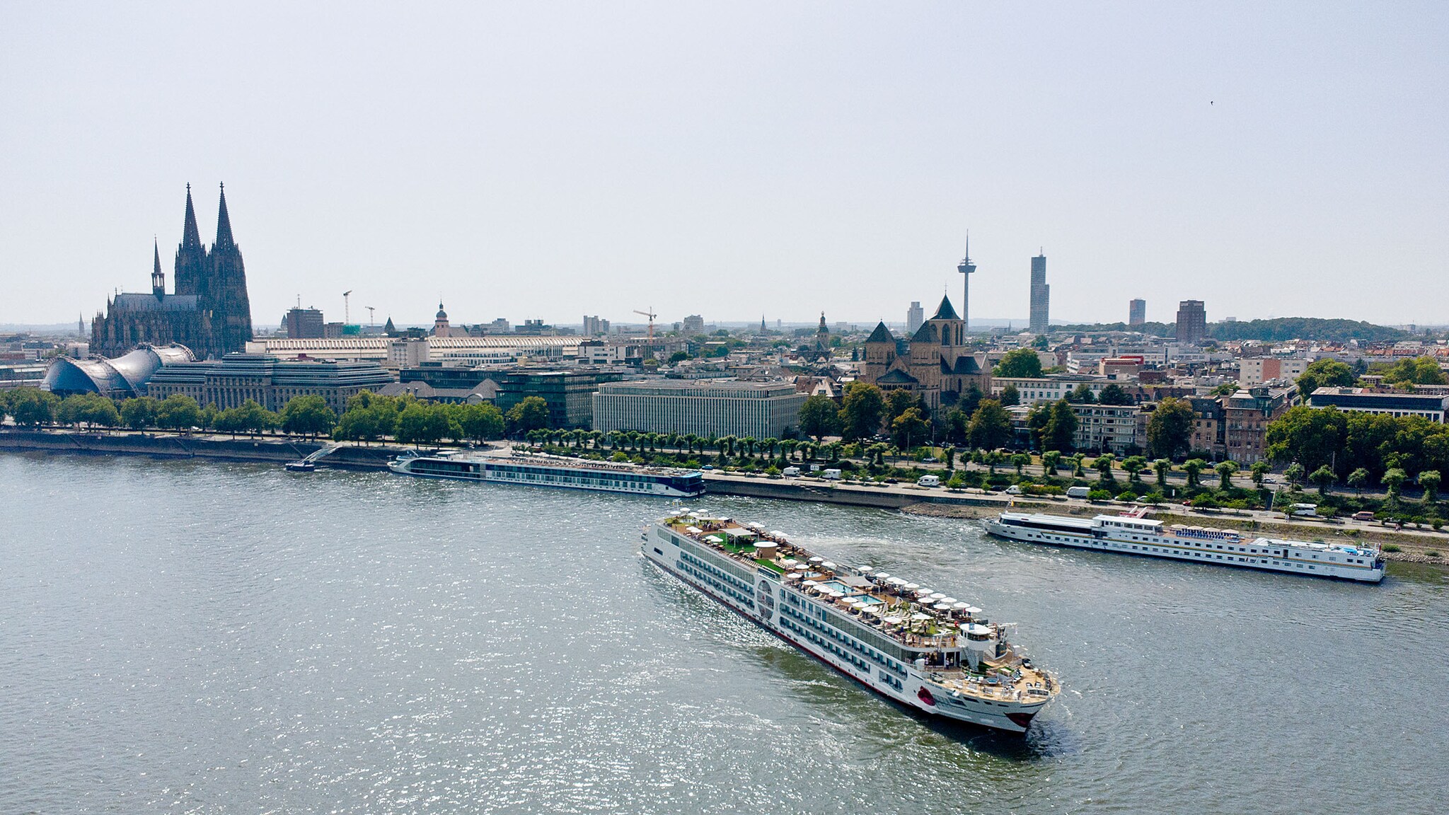Ein Flusskreuzfahrtschiff von A-ROSA fährt auf dem Rhein an der Skyline von Köln vorbei.