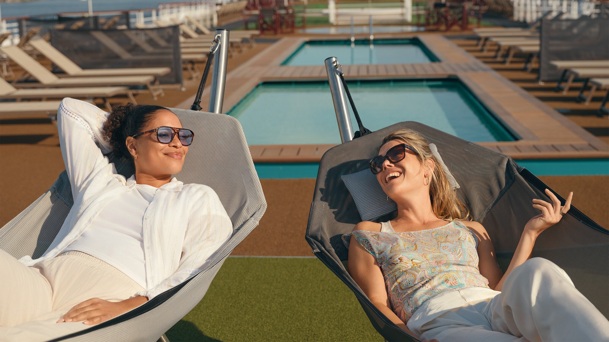 Zwei Frauen liegen auf Sonnenliegen an Deck eines Kreuzfahrtschiffes.