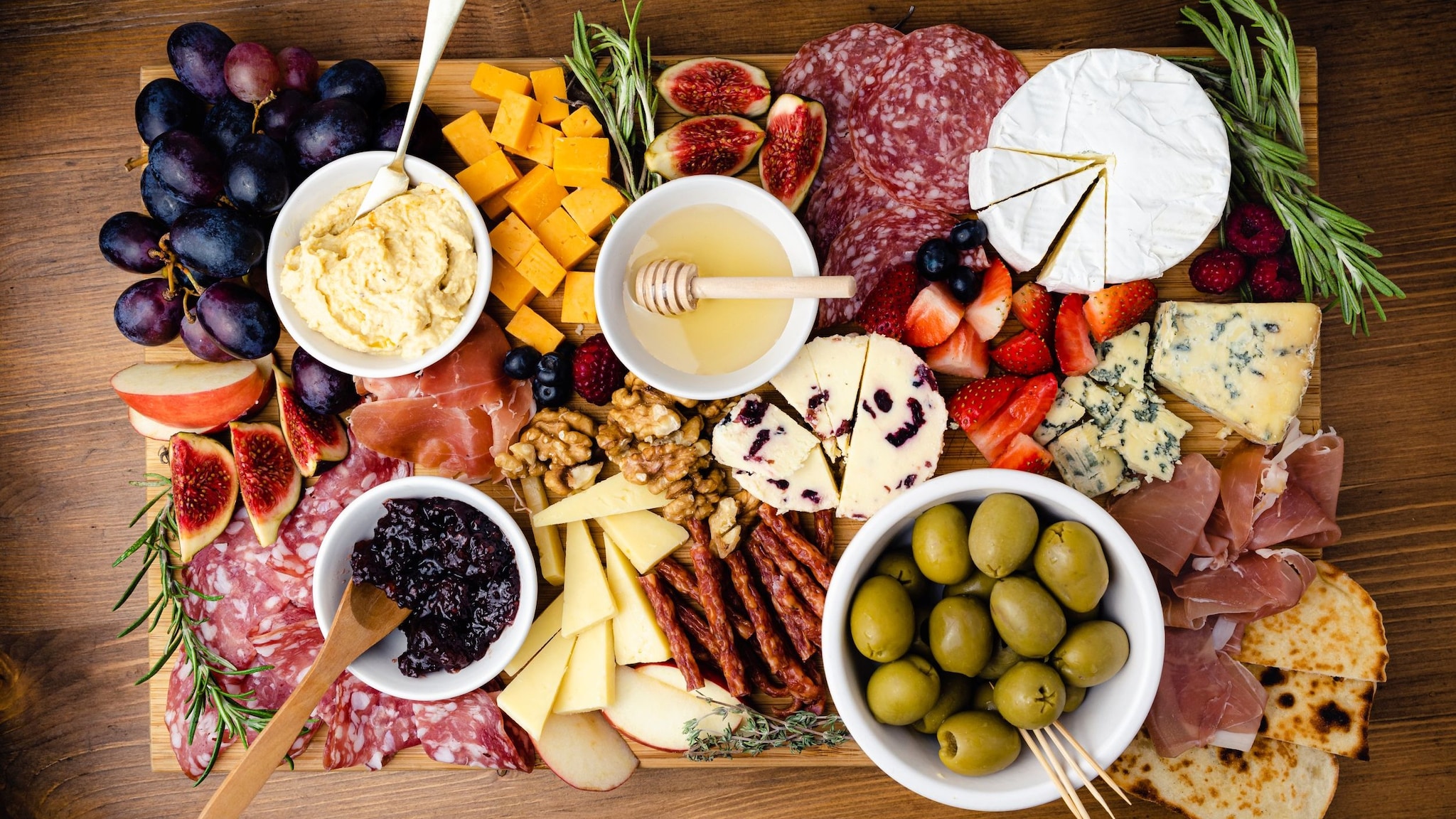 Wurst, Käse, Obst und andere Snacks auf einem Holzbrett von oben.