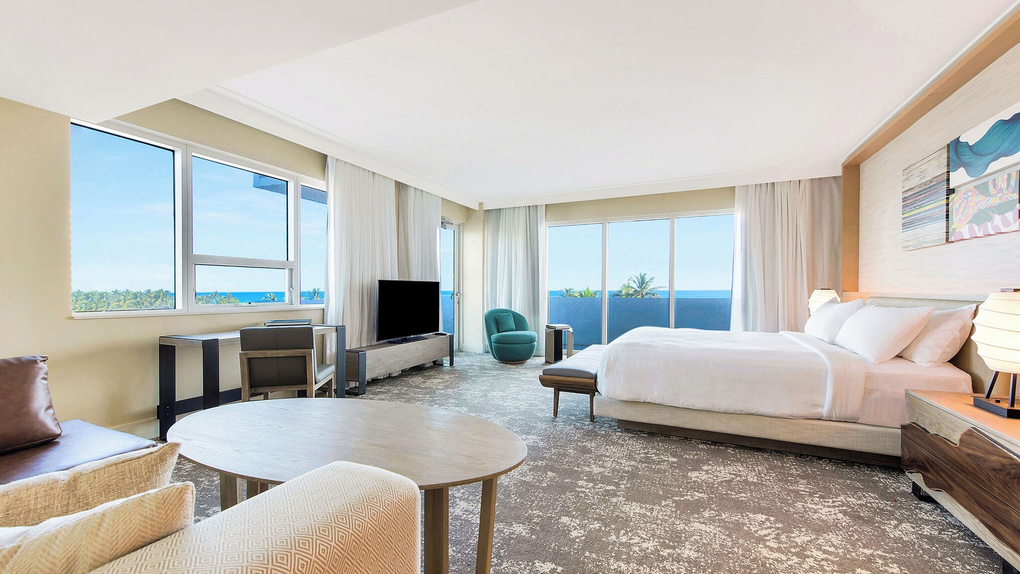 In einem großen, hellen Hotelzimmer steht ein Bett, daneben ein Sessel mit kleinem Tisch.