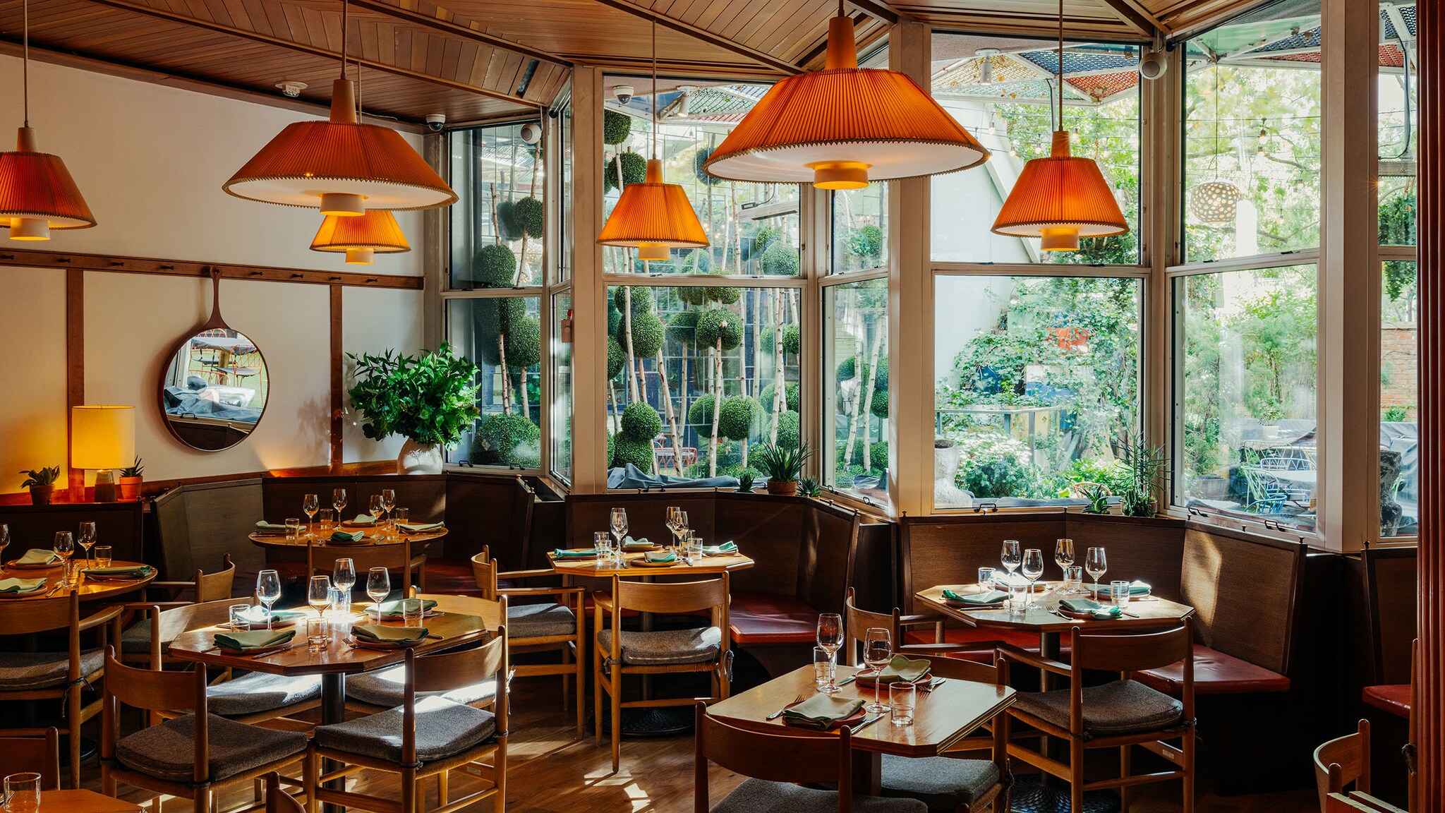 In dem Restaurant eines Hotels stehen gemütlicheSrtühle und Tische vor großen Fenstern mit Blick ins Grüne.