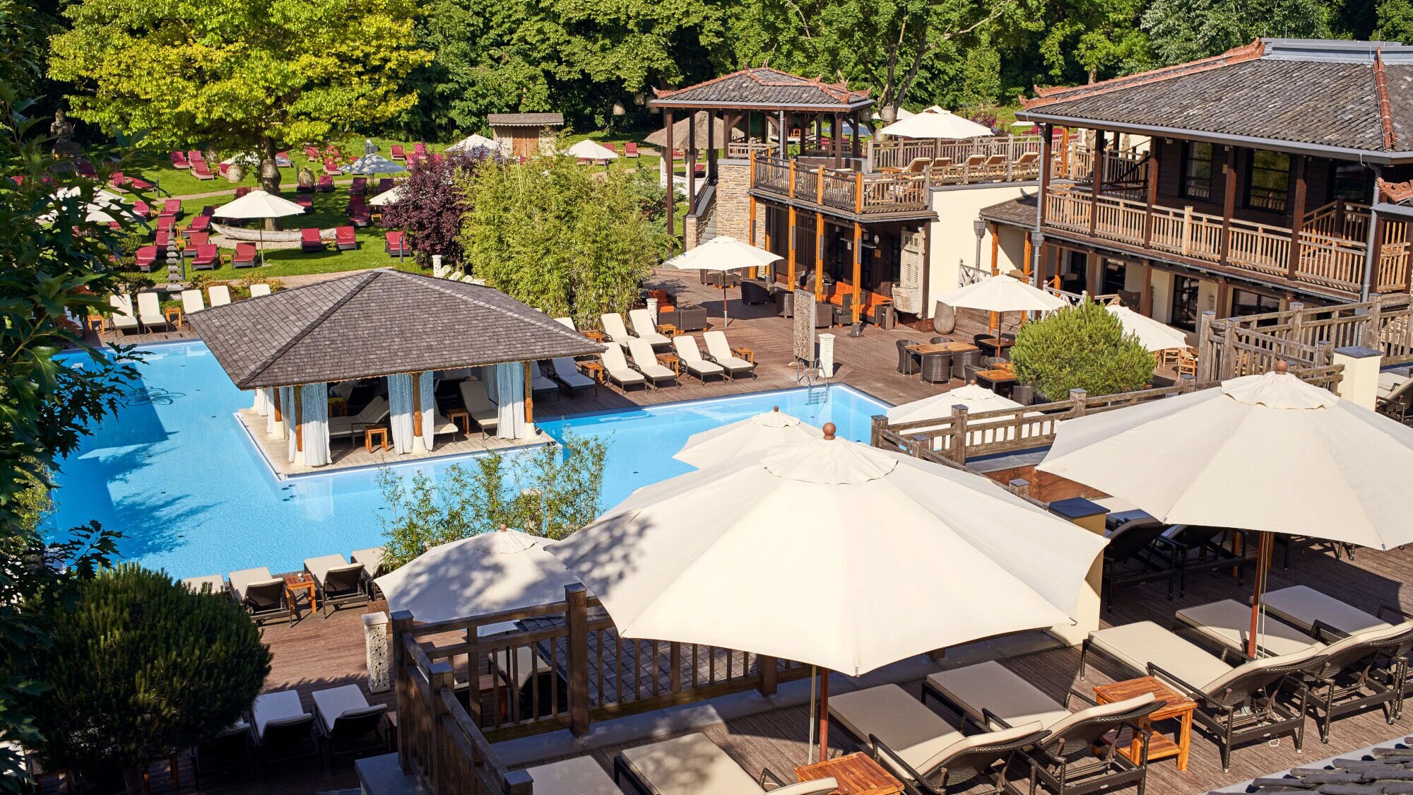Wellnessbereich mit Pool und Sonnenliegen in einem Garten im balinesischen Stil.