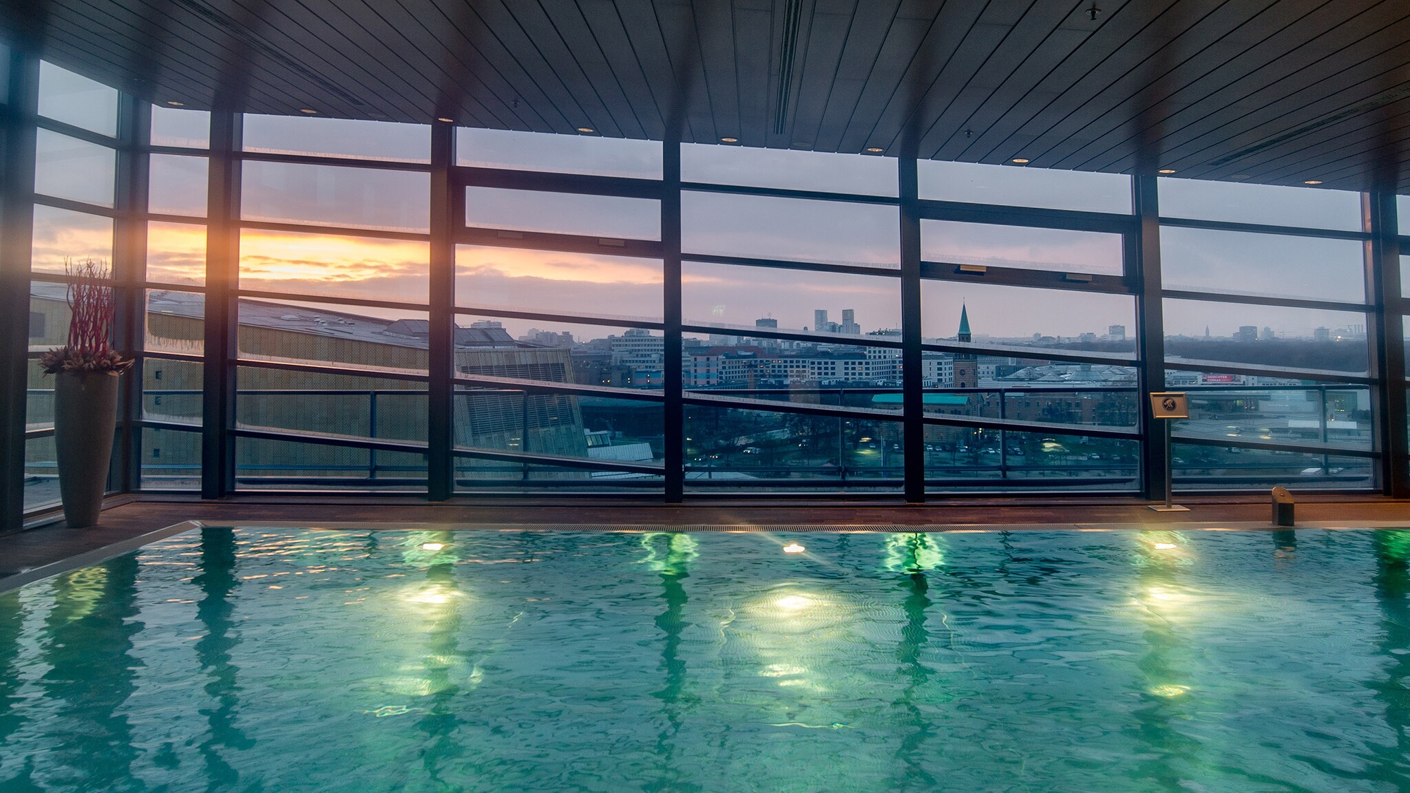 Beleuchteter Indoorpool mit Panoramablick über die Skyline Berlins am Abend.