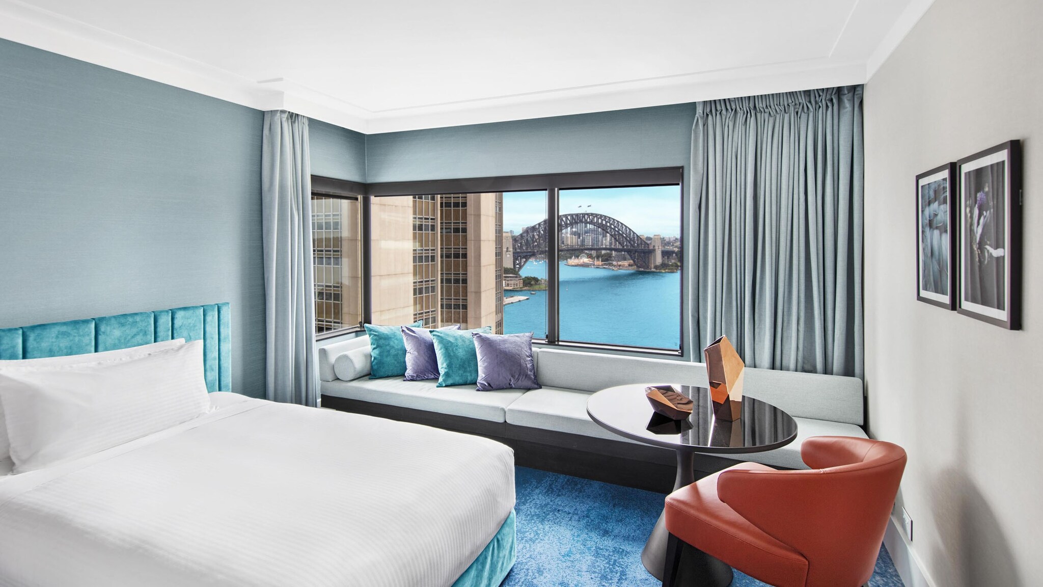 In einem Hotelzimmer steht ein Bett und ein Sofa vor einem großen Fenster mit Blick auf eine Skyline.