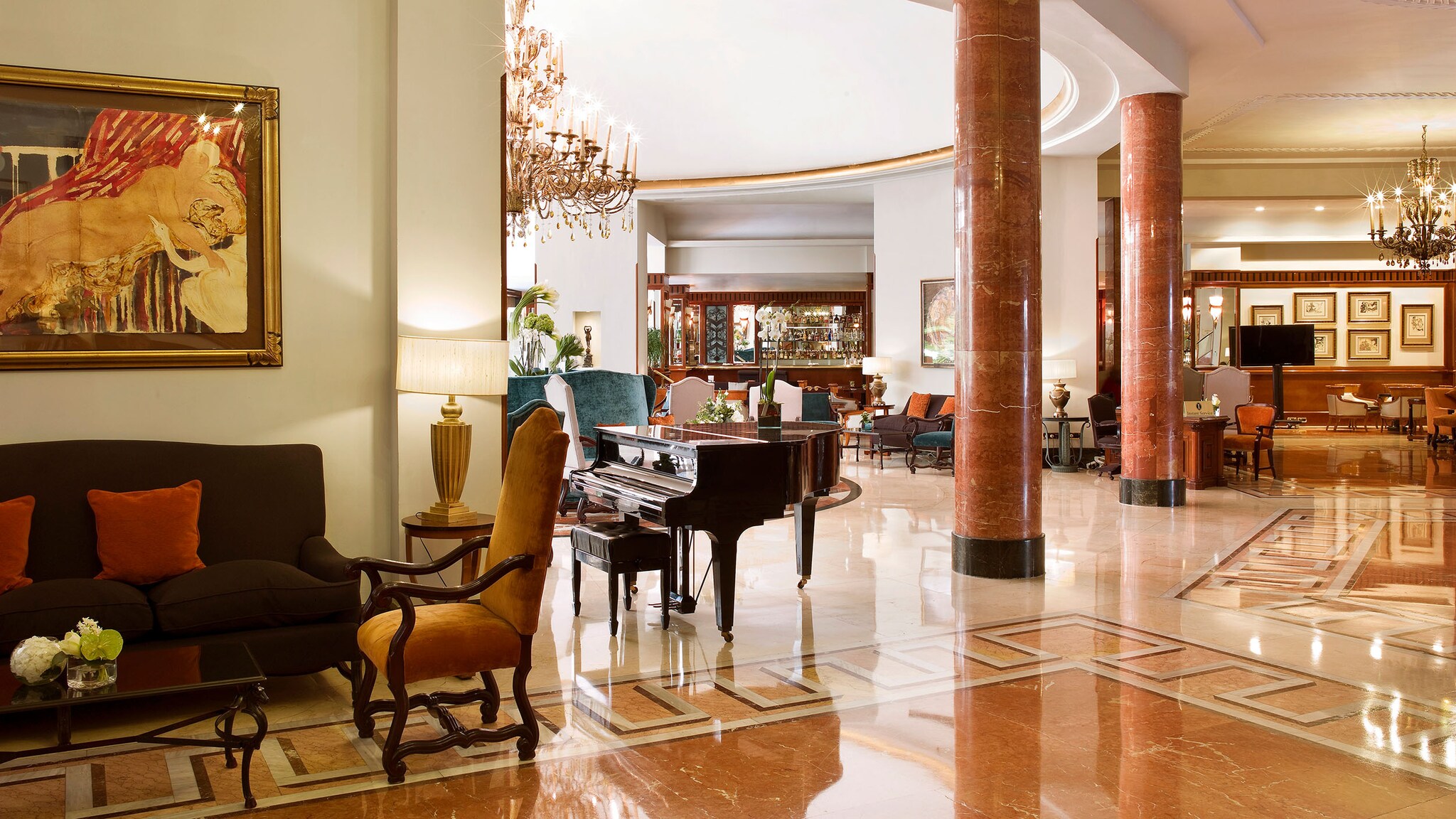 In einer Hotel-Lobby stehen Marmorsäulen neben einem Klavier und Sesseln.