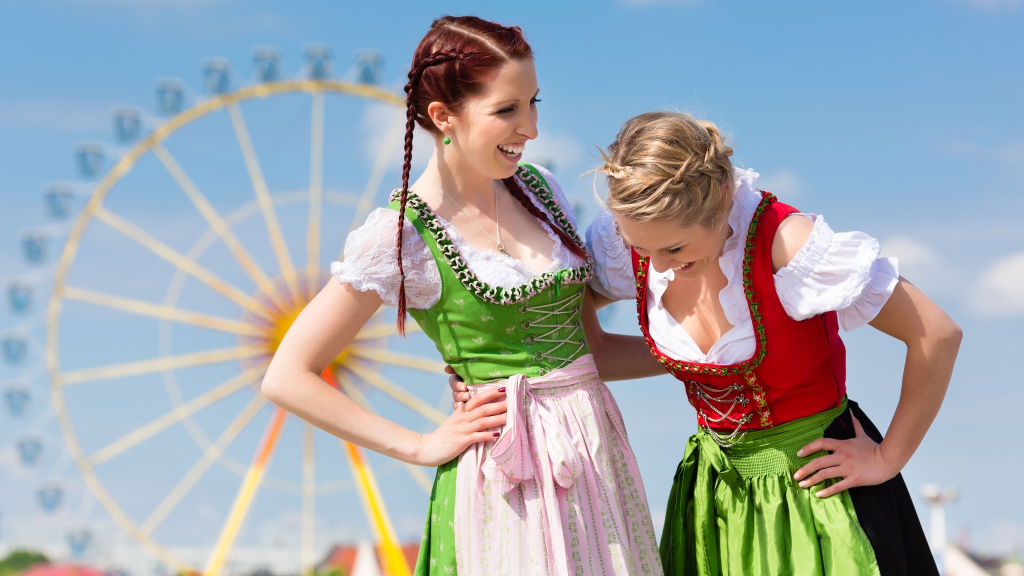 Zwei Frauen tragen Dirndl mit Schürze und Rock und lachen sich an.