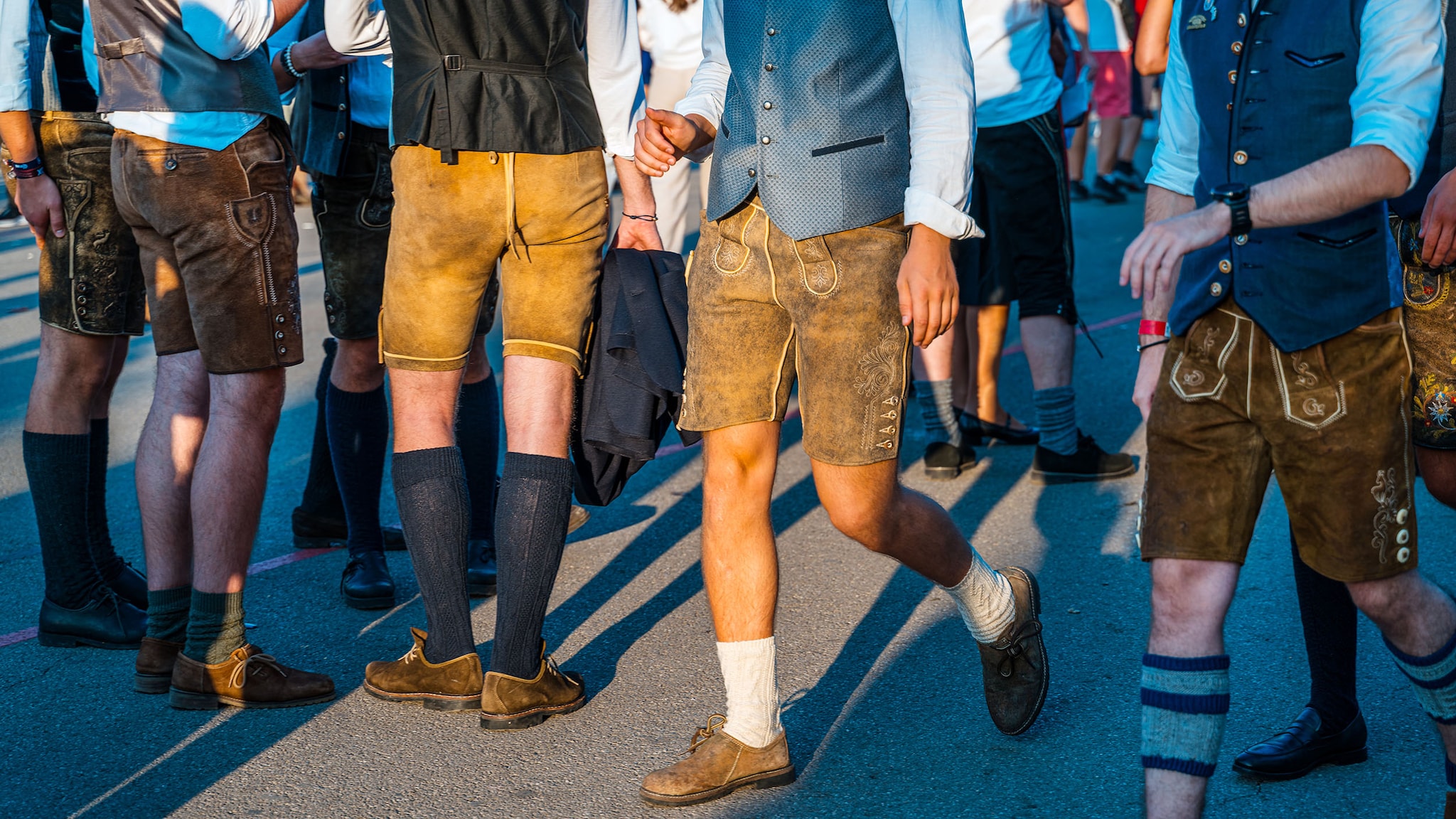 Auf einem Festplatz stehen Männer mit Lederhosen, Westen und Haferlschuhen.