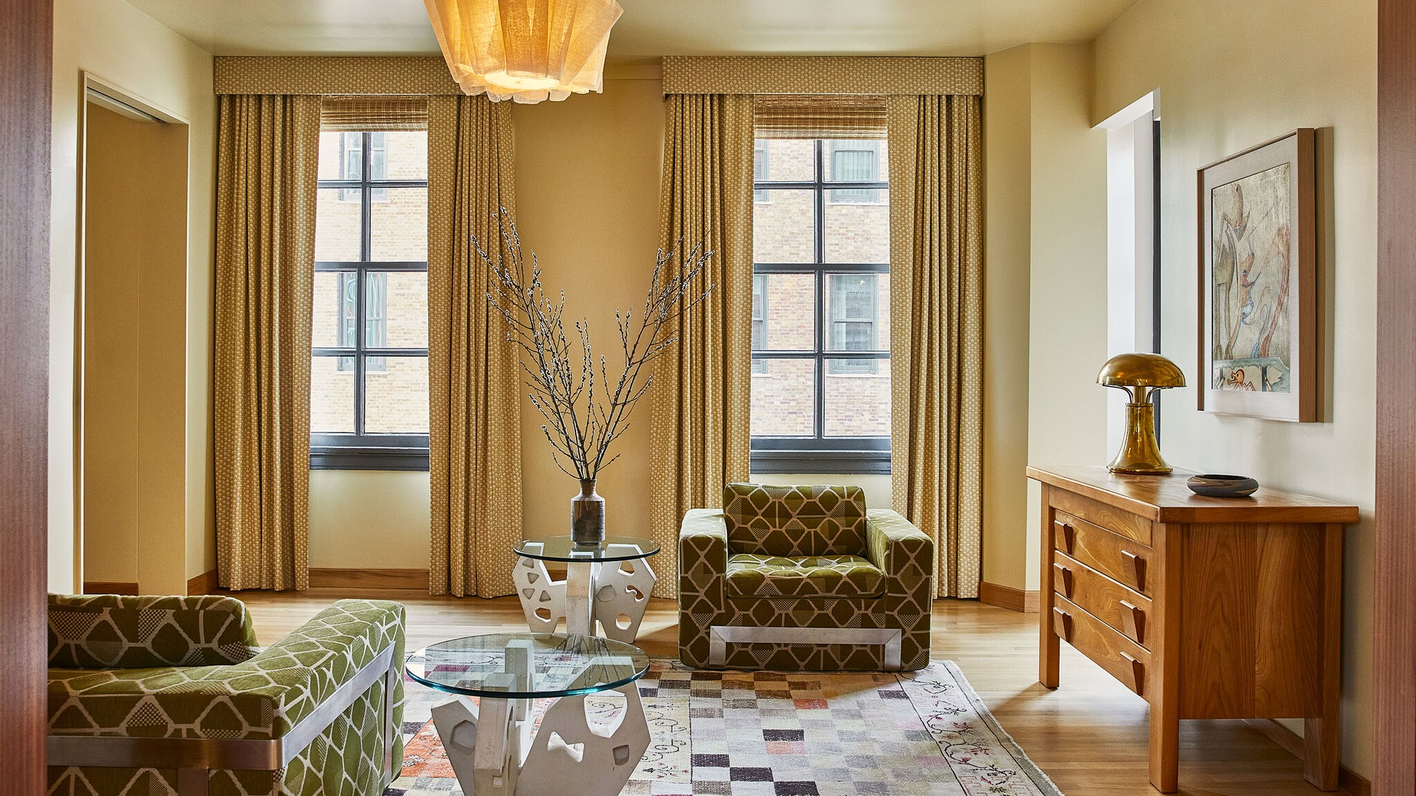 In einem Hotelzimmer steht ein bunter Sessel, auf einem großen Teppich und an der Wand hängt ein Kunstwerk.