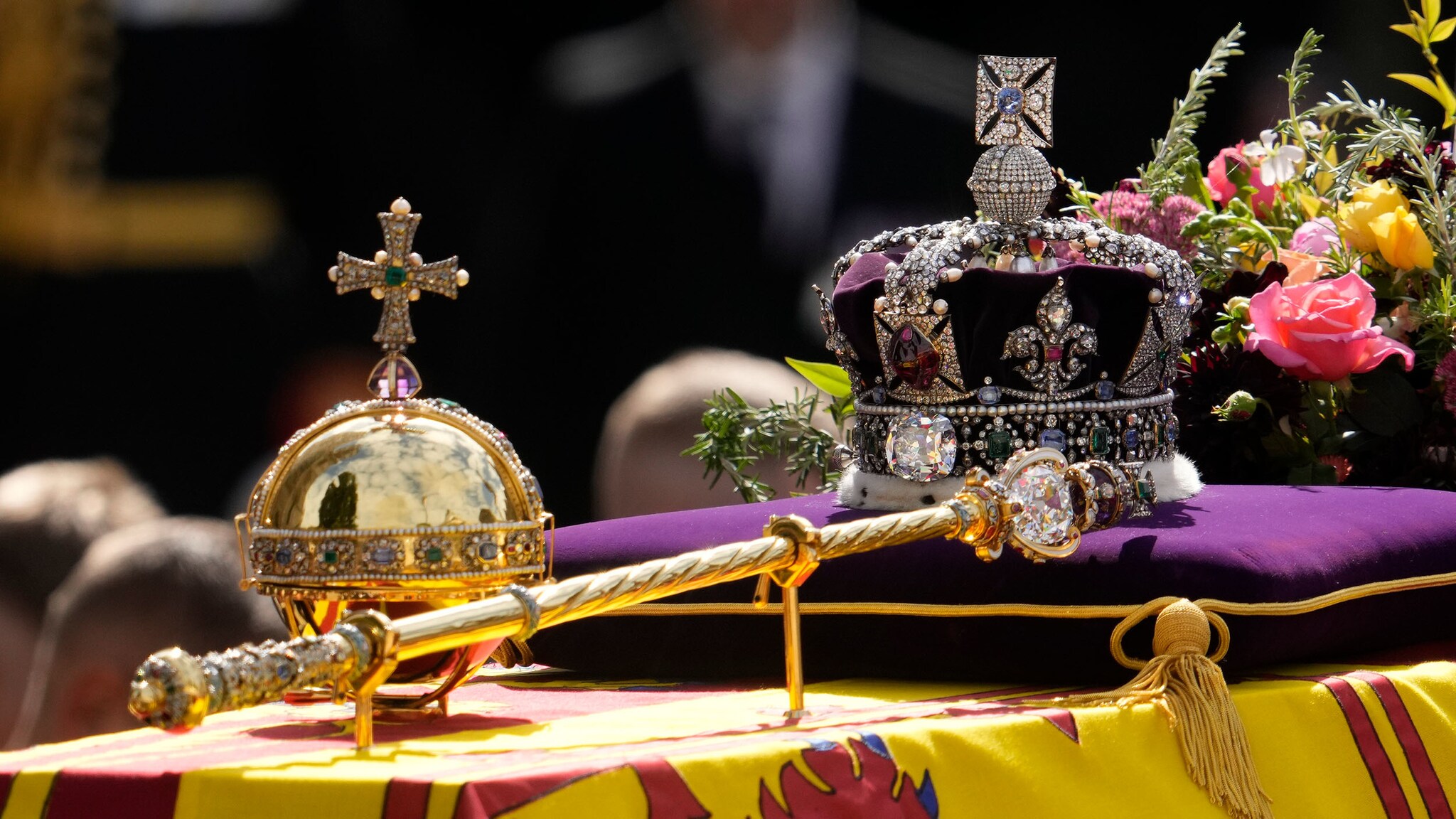 Auf einem Tuch und einem Kissen liegen drei Kronjuwelen: die Imperial State Crown, das königliche Zepter und der Sovereign's Orb.