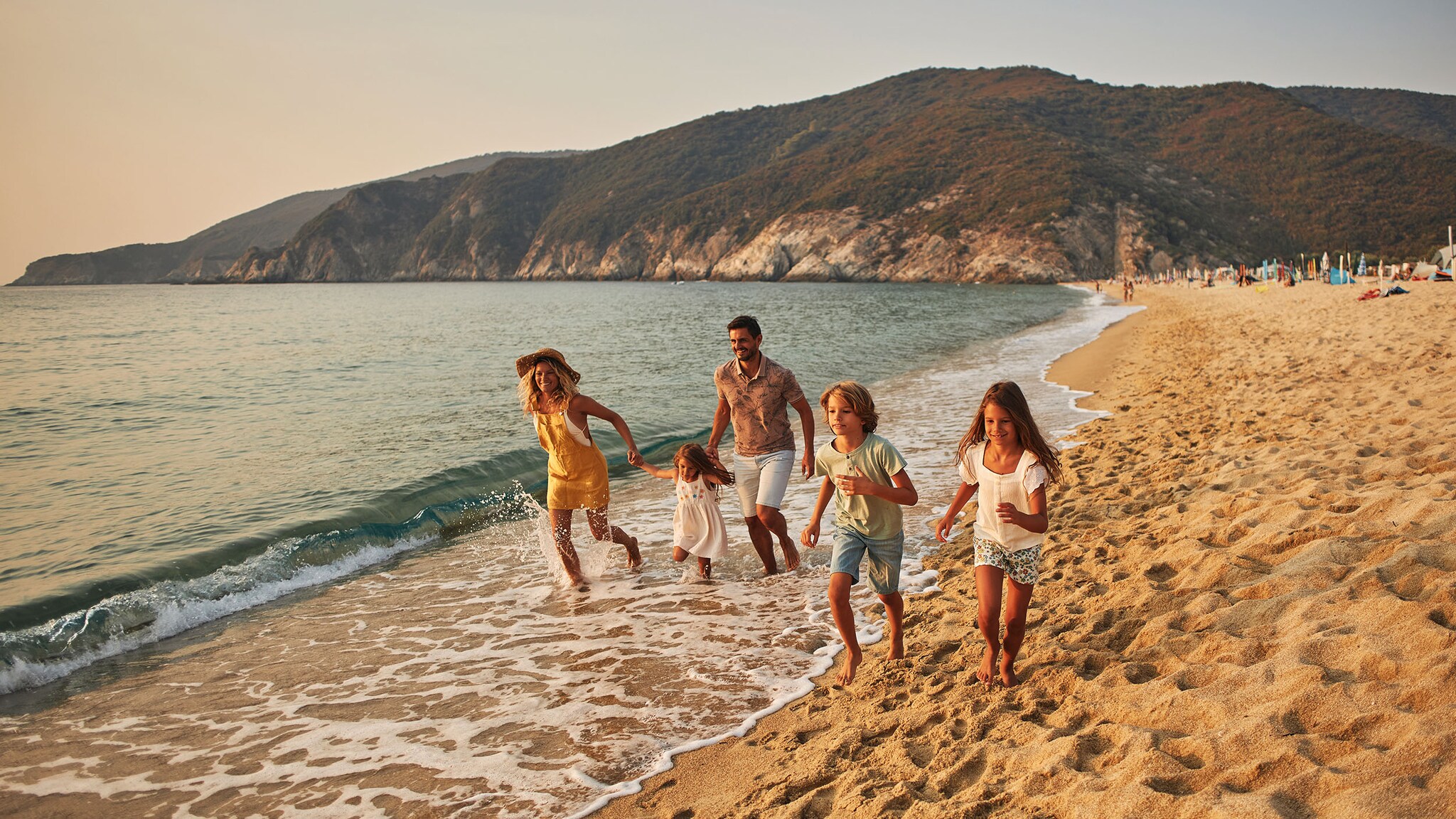Eine Familie mit zwei Kindern läuft in Sommerkleidung fröhlich an einem Sandstrand entlang.