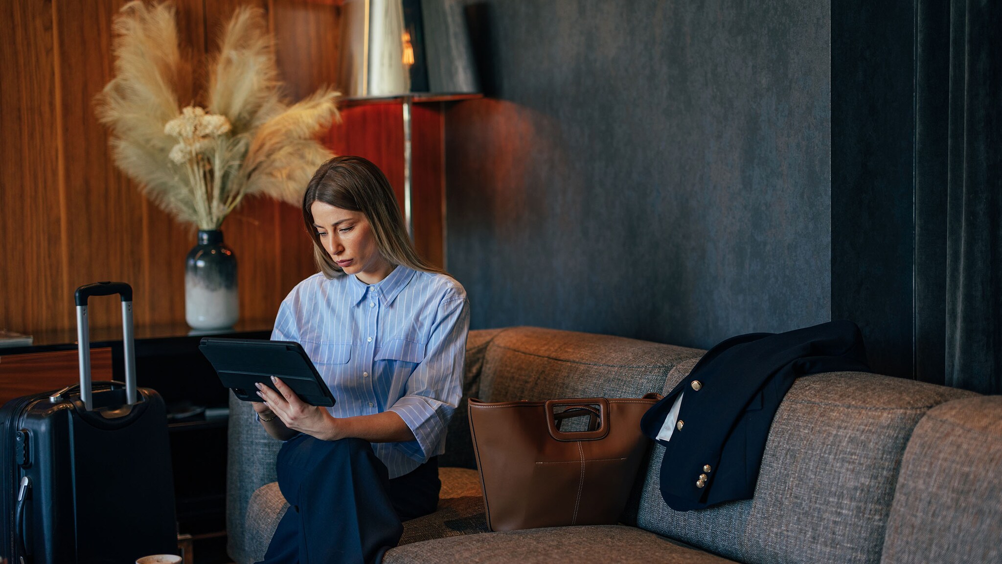 Eine Frau sitzt in einem Hotel auf einem Sofa und schaut in ein Tablet.
