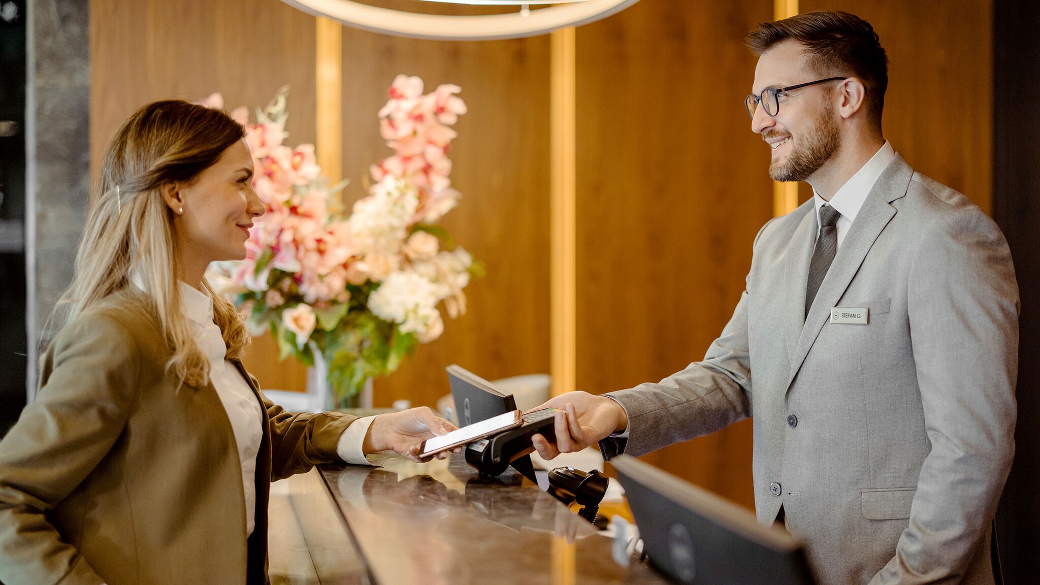 American Express und Google Pay Eine Frau bezahlt mit ihrem Smartphone an einer Hotelrezeption.