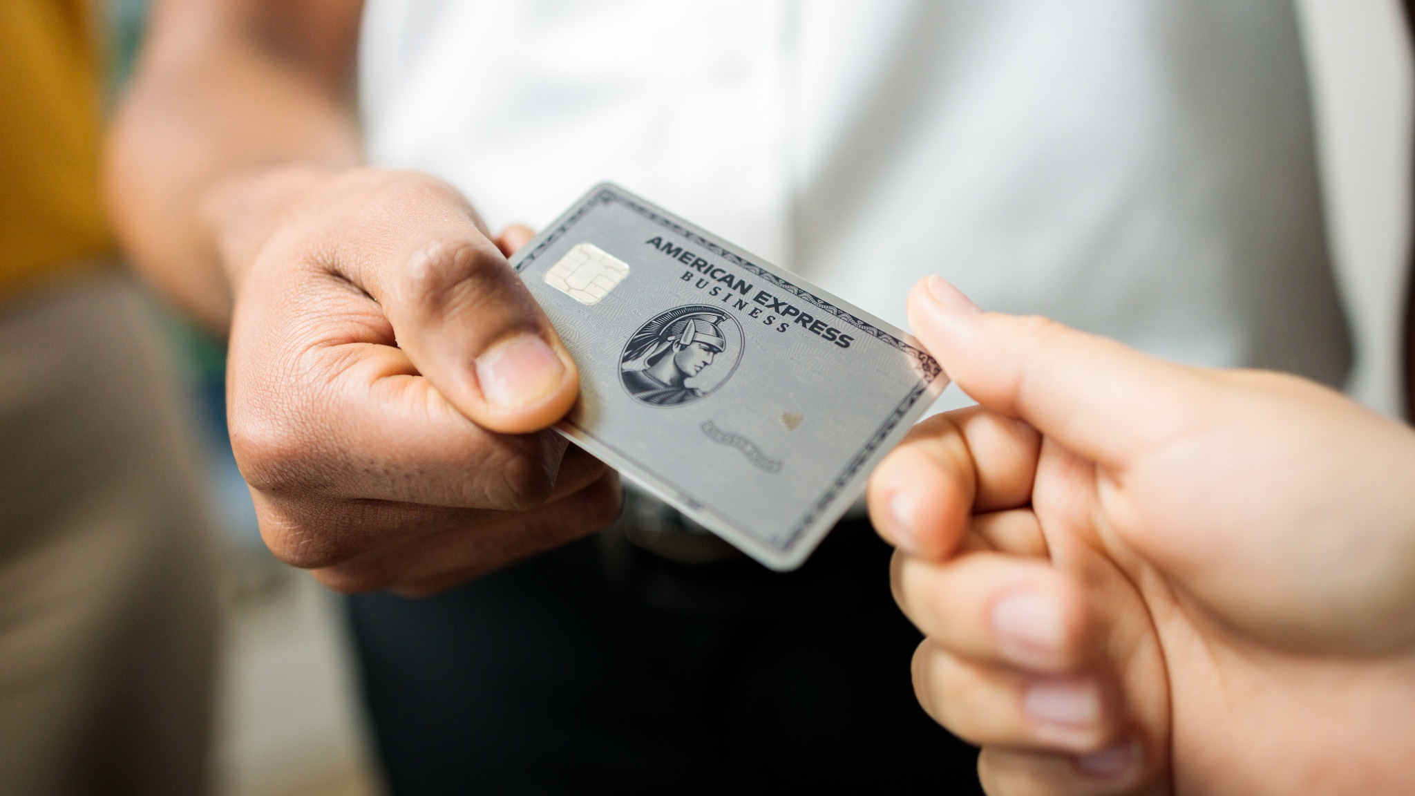 Nahaufnahme einer silbernen Kreditkarte von American Express zwischen den Händen zweier Personen.