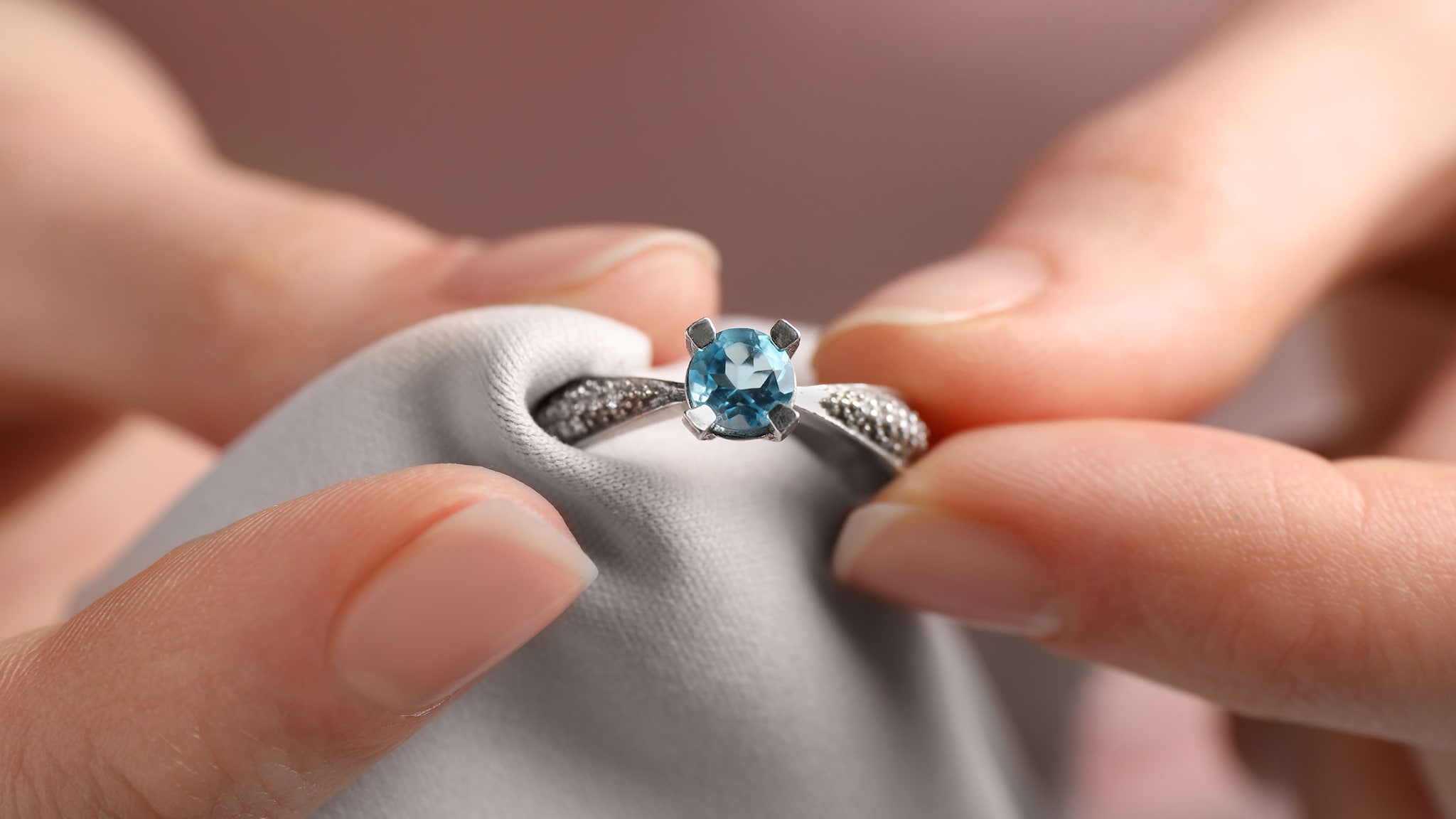 Eine weibliche Hand hält einen Ring mit einem hellblauen Diamanten.