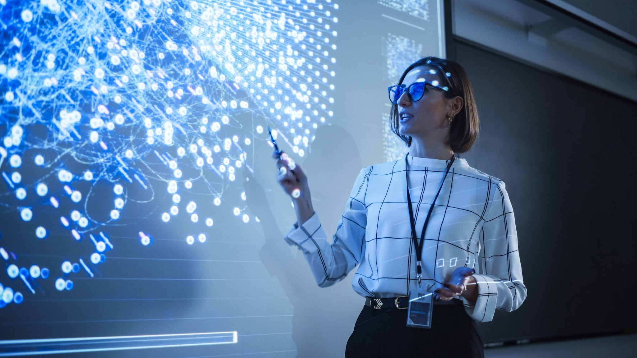 amex-sbs-business-model-disruption-frau Eine stehende Frau hält eine digitale Präsentation im blauen Licht der Projektion einer Datenvisualisierung.