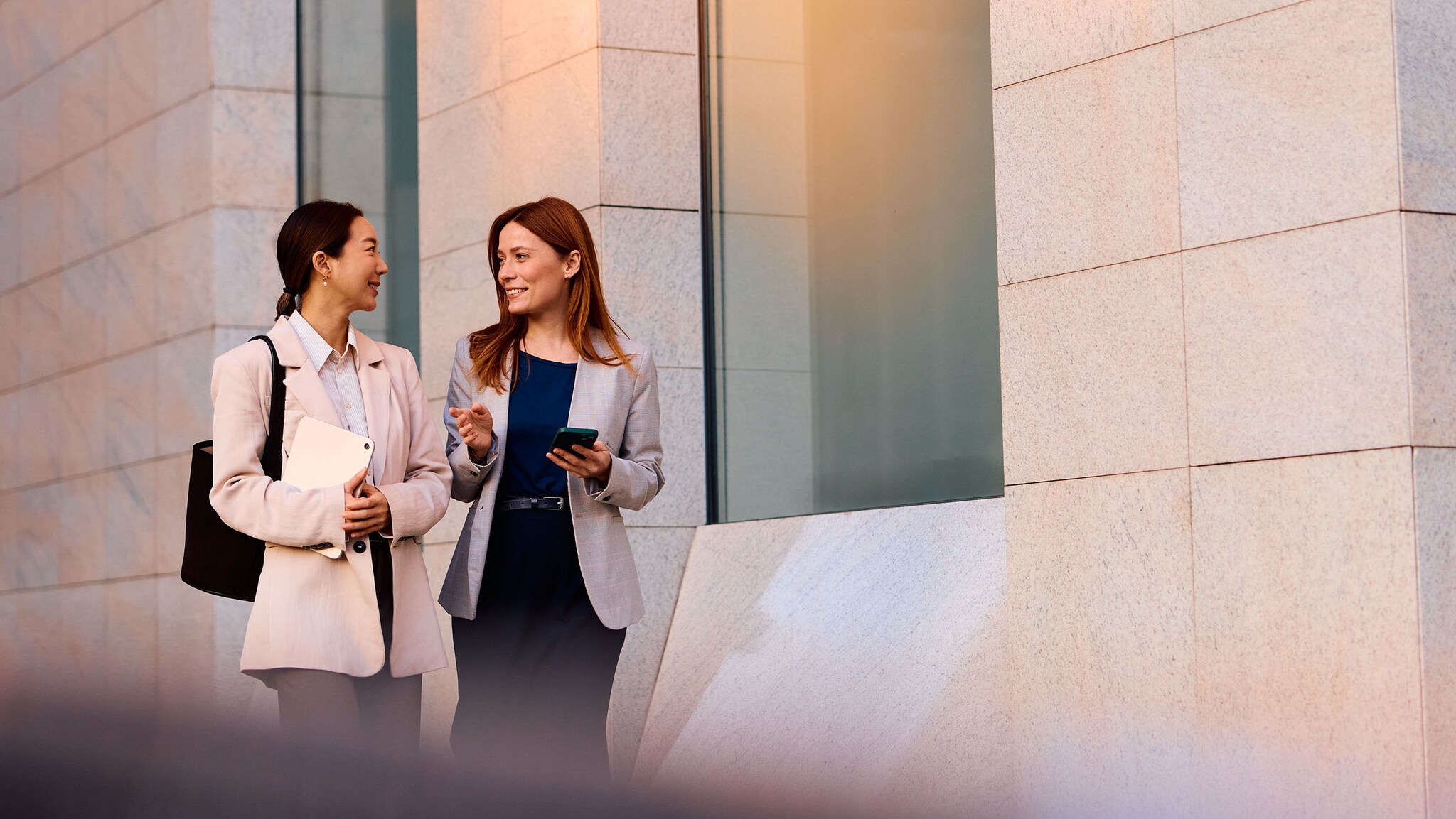SBS MGM Zwei Frauen in Business-Kleidung laufen eine Straße entlang und unterhalten sich.