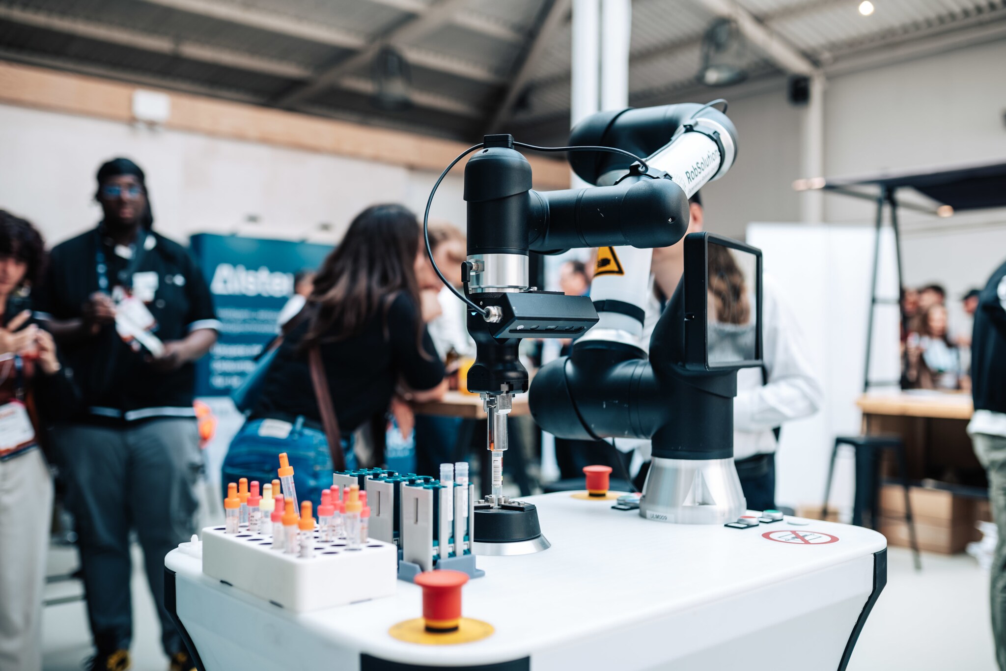 Ein Roboterarm operiert an einem Messestand mit verschiedenen Reagenzgläsern.