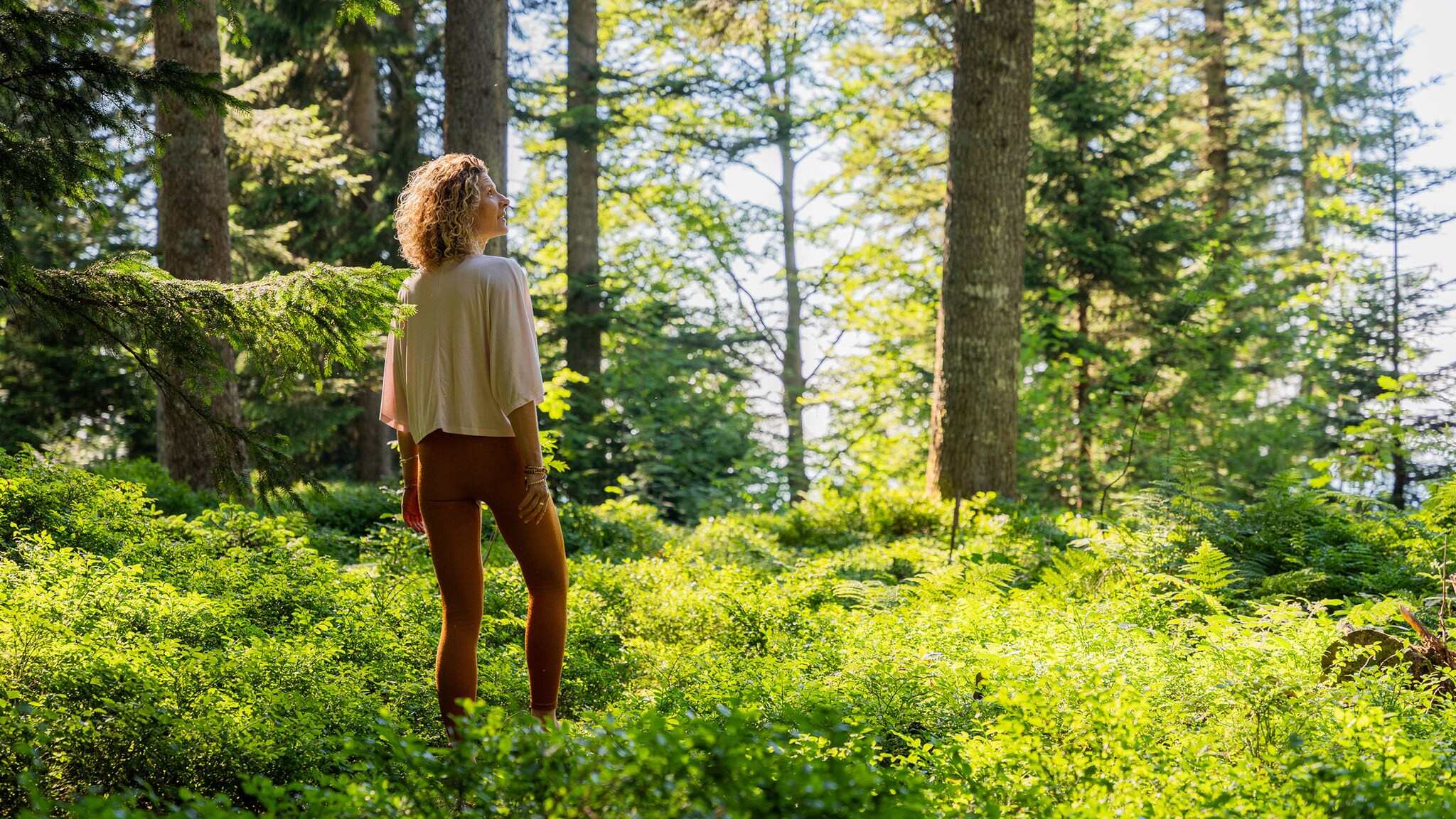 Eine Frau steht in einem grünen Wald und schaut in die Ferne.