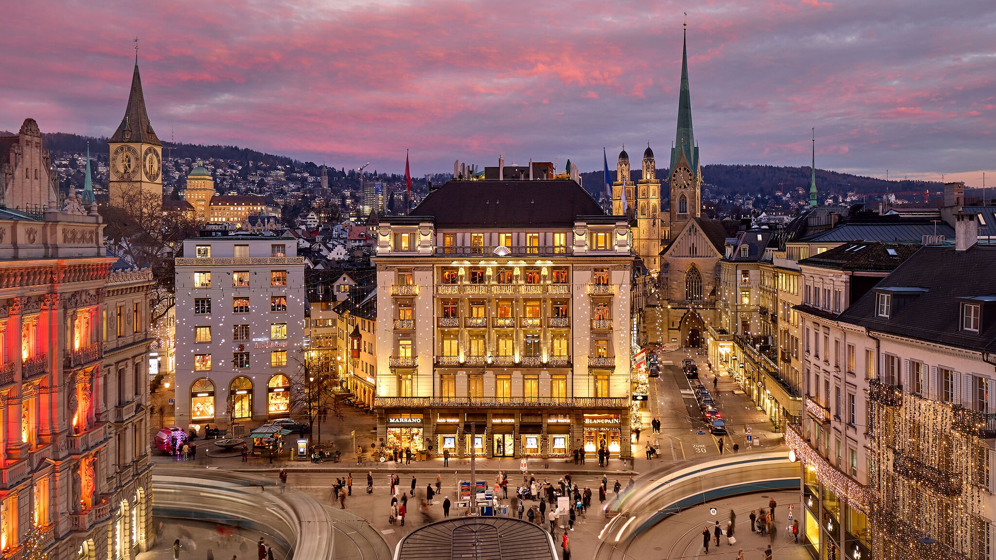 Auf dem Paradeplatz in Zürich steht ein großes historisches Hotel, das beleuchtet ist.