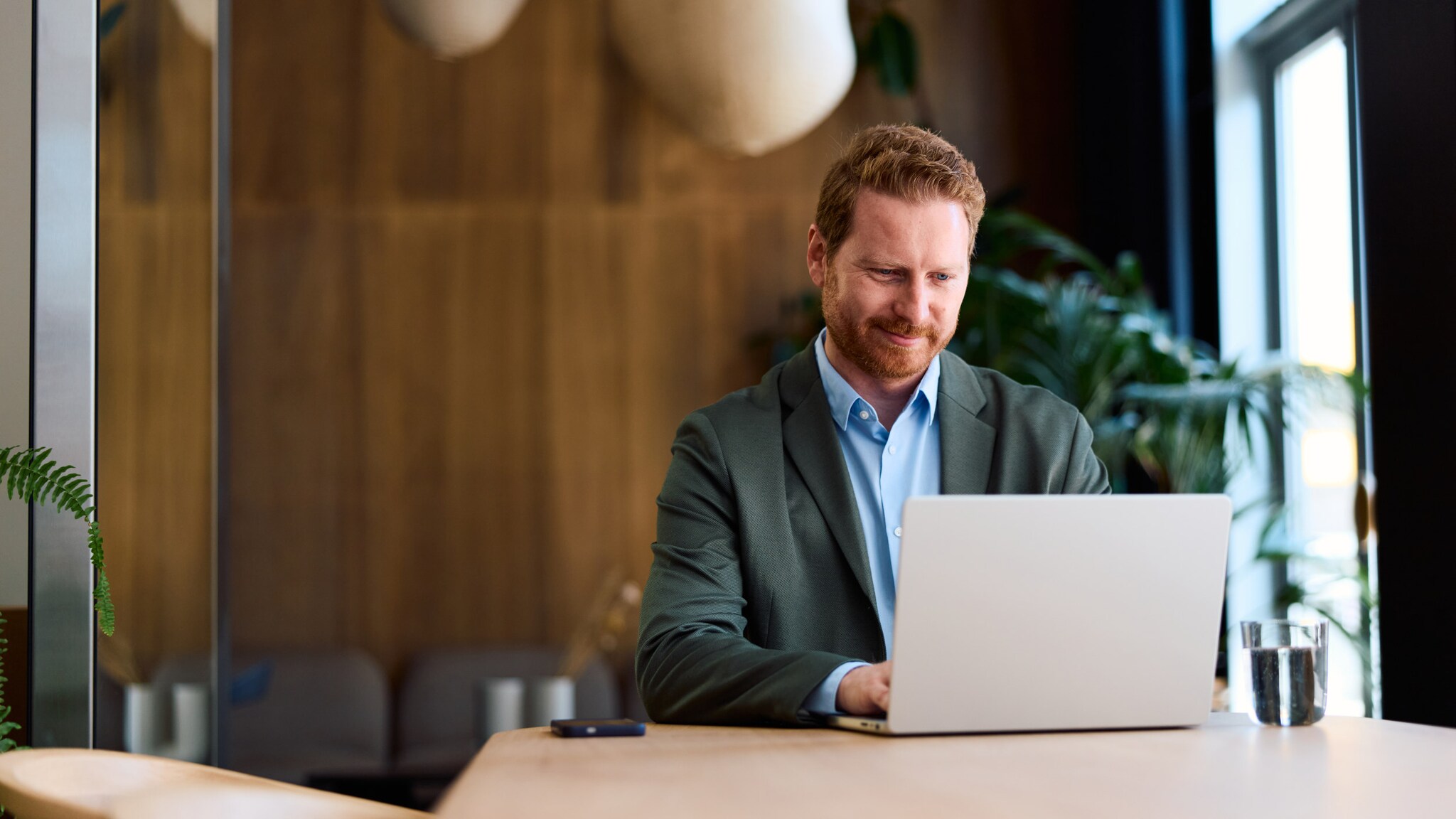Ein Mann in Business-Kleidung sitzt an einem Tisch an einem aufgeklappten Laptop.