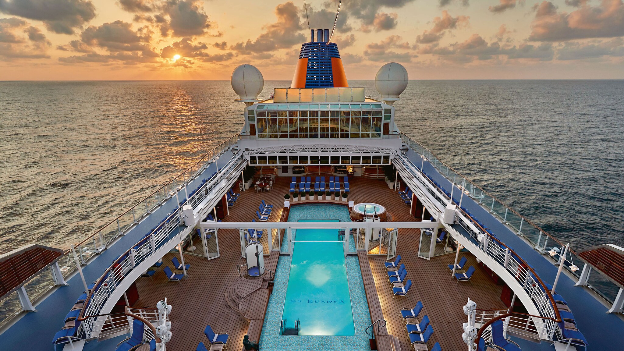 Aufsicht eines Pooldecks auf einem kleinen Kreuzfahrtschiff auf offenem Meer bei Sonnenuntergang.
